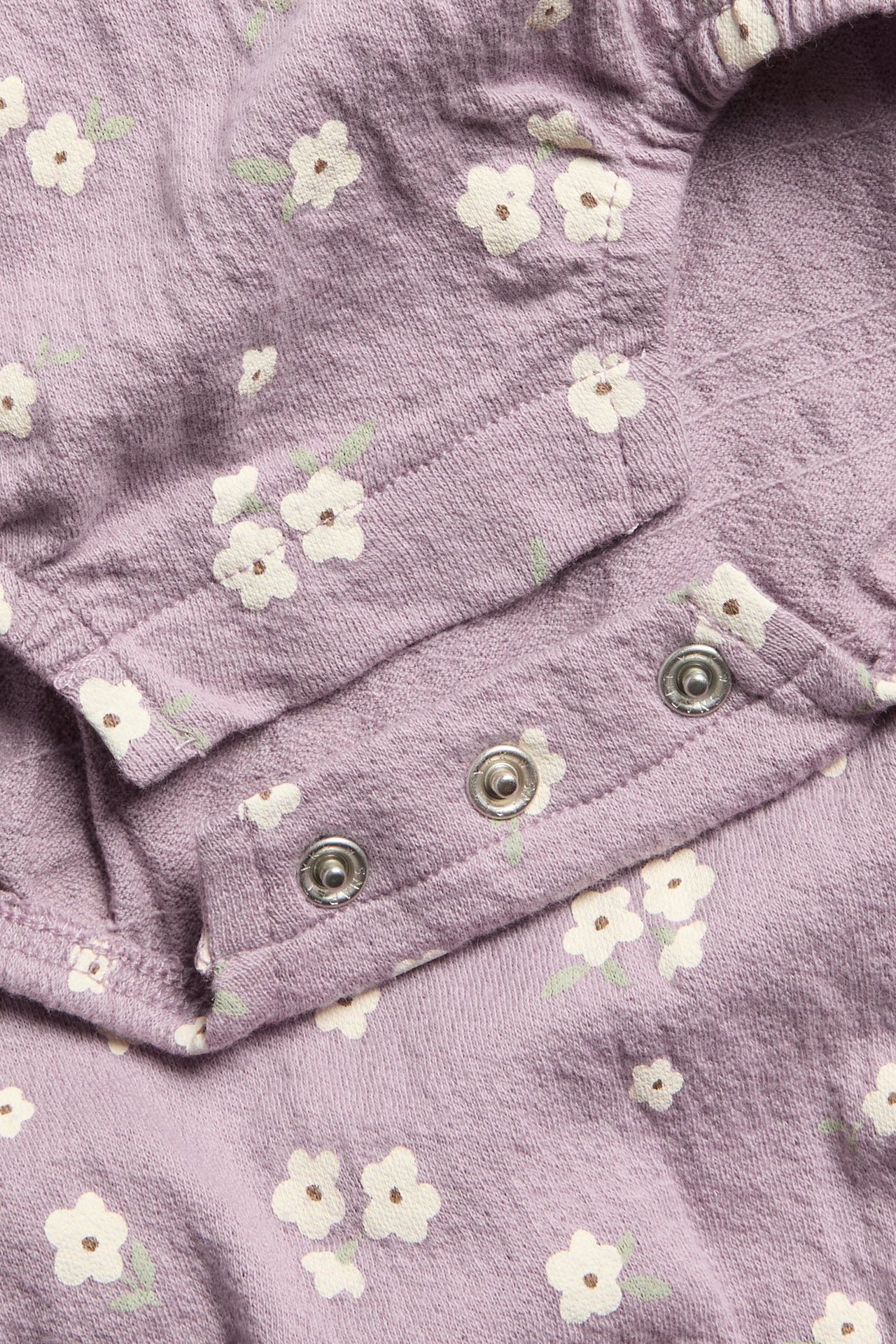 Zbliżenie liliowego body niemowlęcego w kwiaty z widocznymi zatrzaskami.