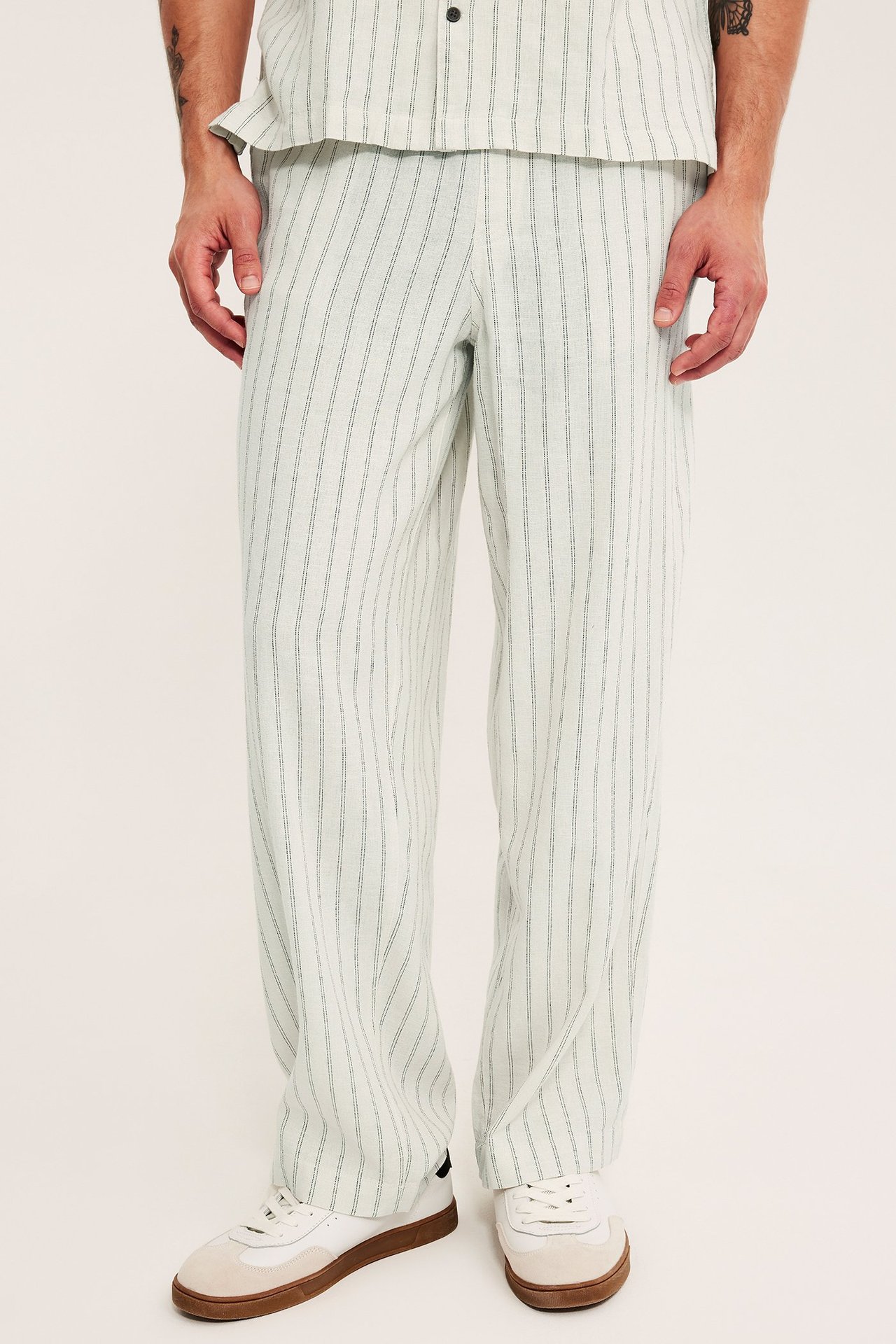 Miehen edestä: beiget raidalliset pellava-viskoosi pull-on housut, yhteensopiva paita ja valkoiset tennarit.