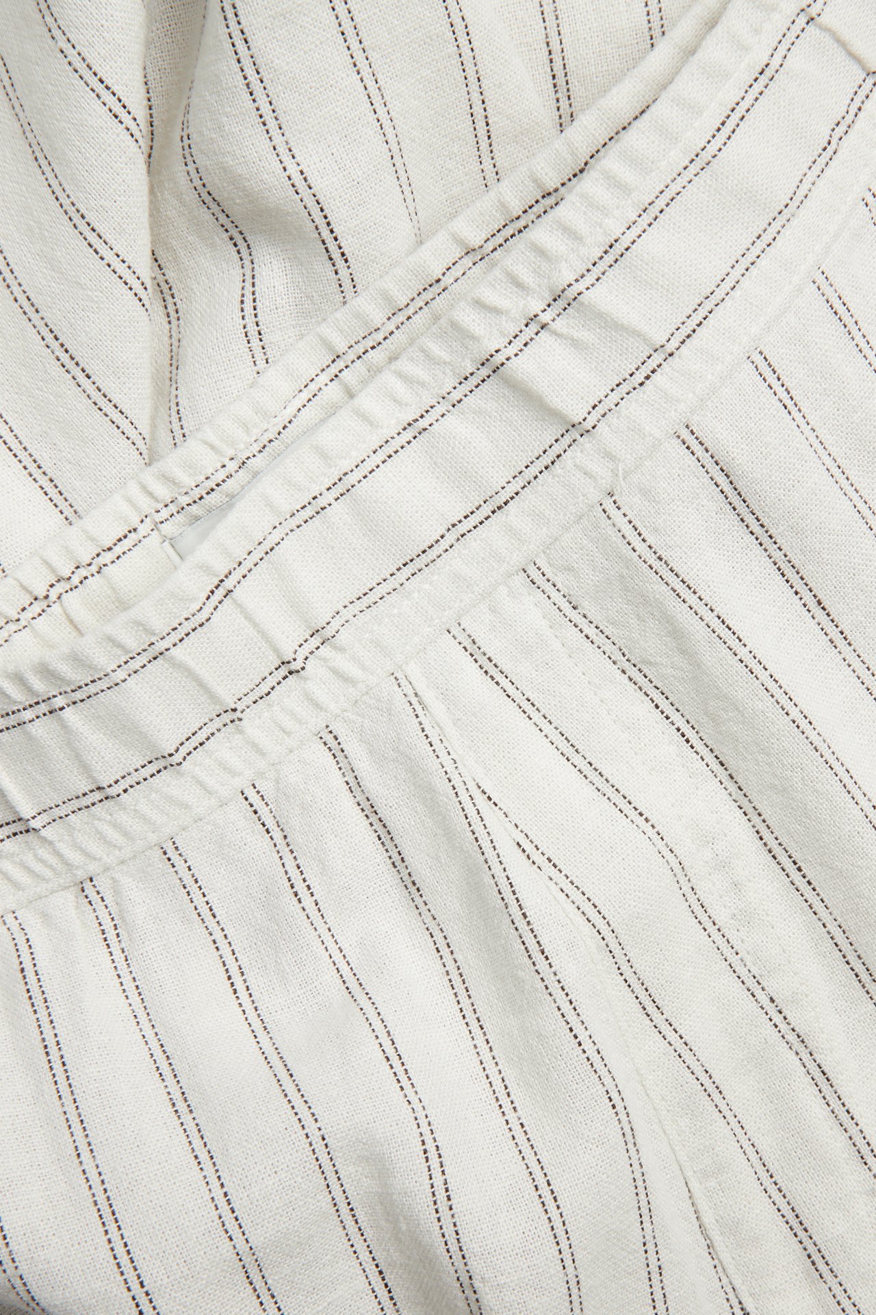 Nærbilde av beige stripete bukser i lin- og viskoseblanding med elastisk linning.