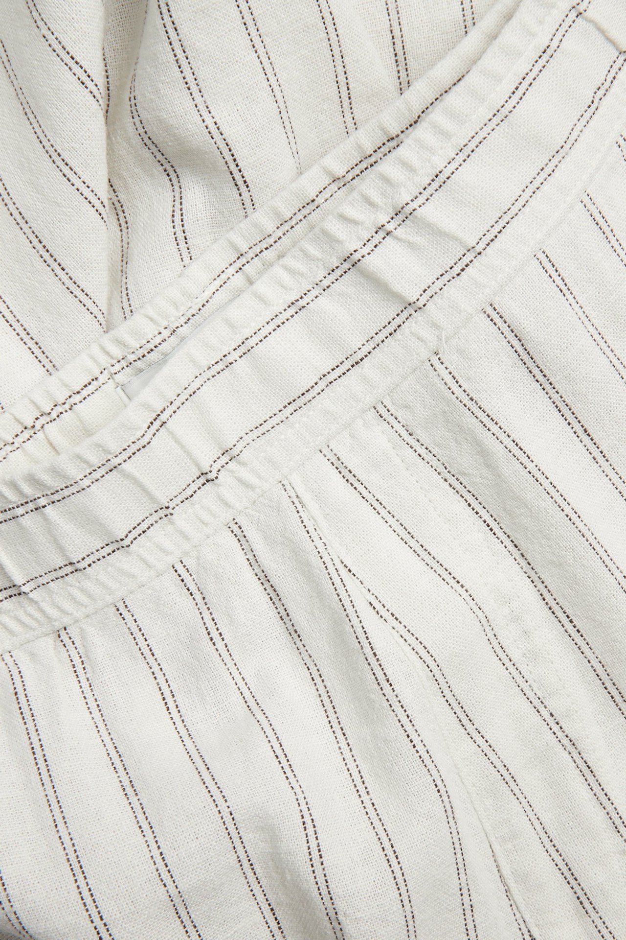 Zbliżenie beżowych, pasiastych spodni z mieszanki lnu i wiskozy z elastyczną talią.