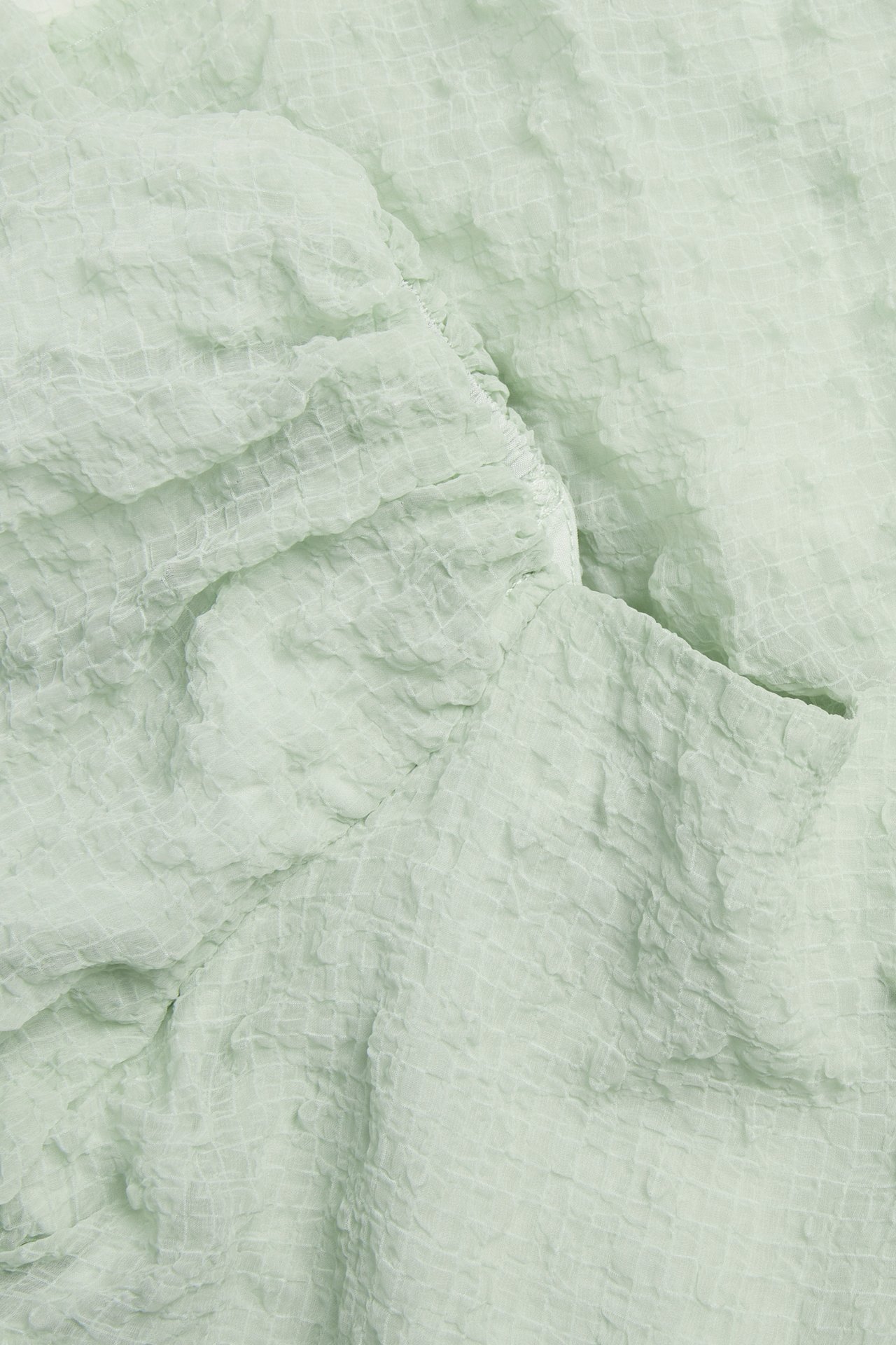 Lähikuva vaaleanvihreästä, strukturoidusta sifonkikankaasta mekosta, jossa on hienovarainen ruudukuvio.