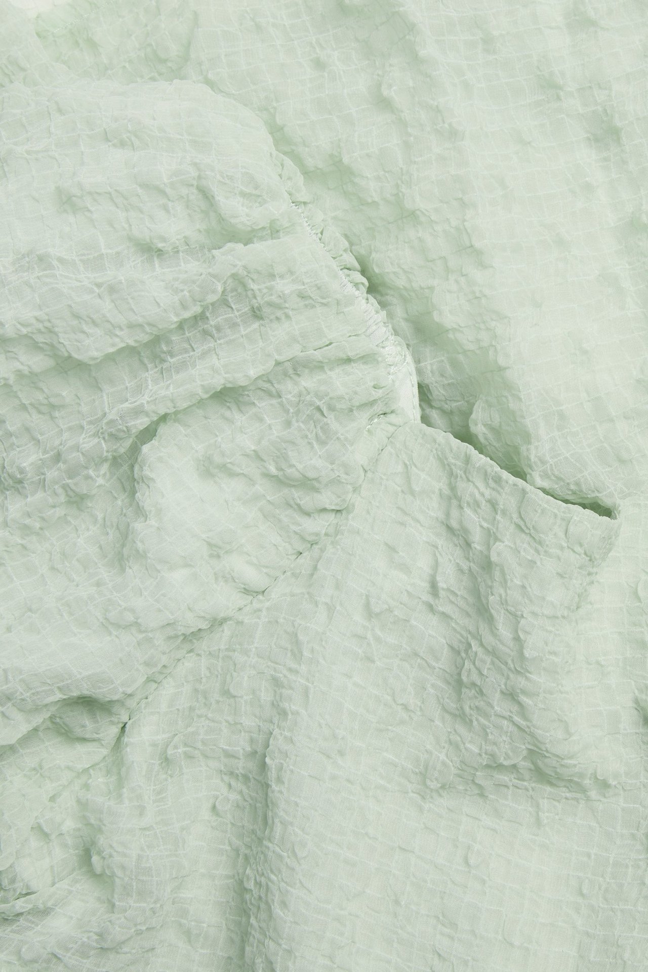 Zbliżenie na jasnozielony, strukturalny szyfon sukienki z subtelnym wzorem w kratę.