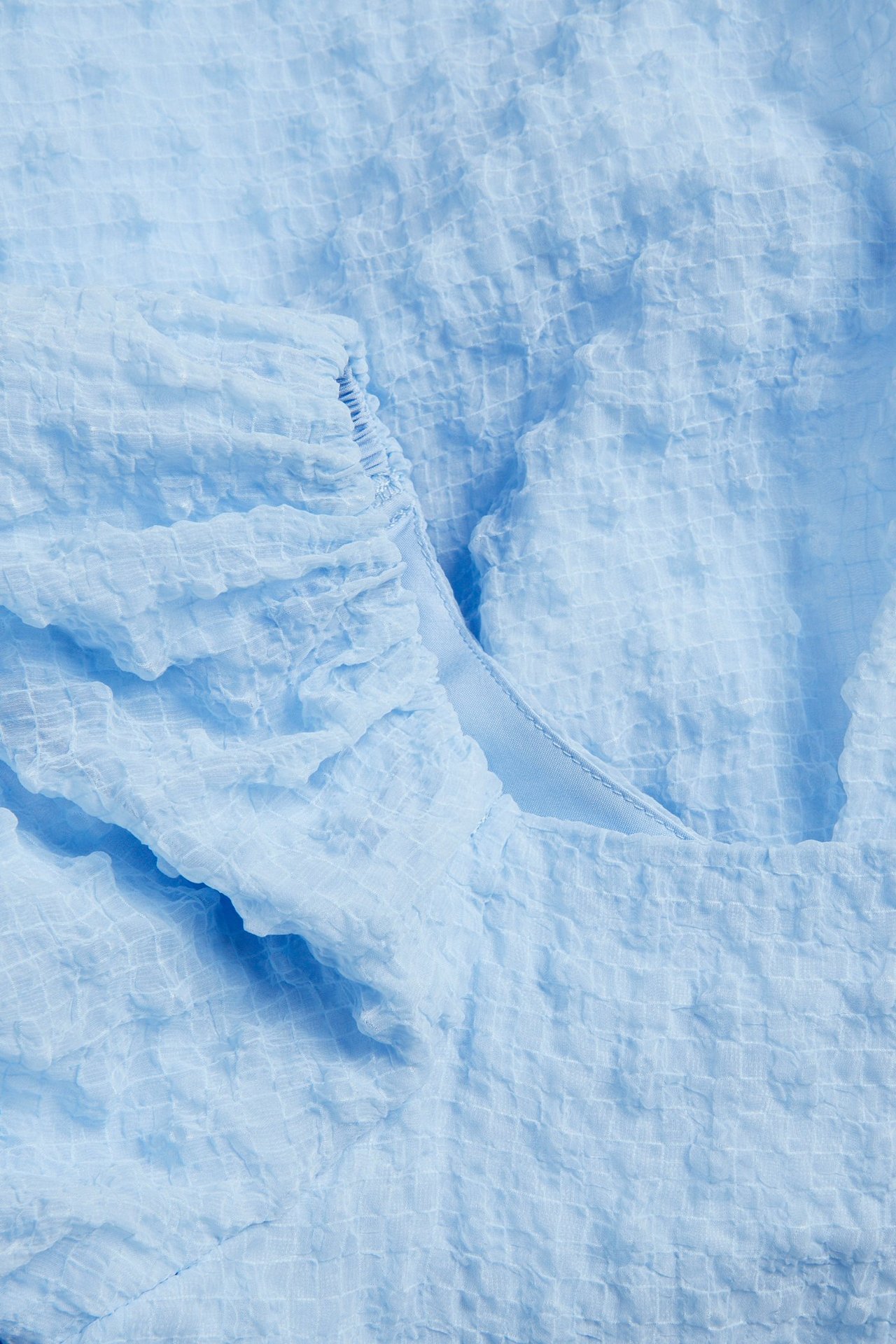Zbliżenie na jasnoniebieską, obszerną sukienkę szyfonową z teksturowanej tkaniny i marszczonymi detalami.