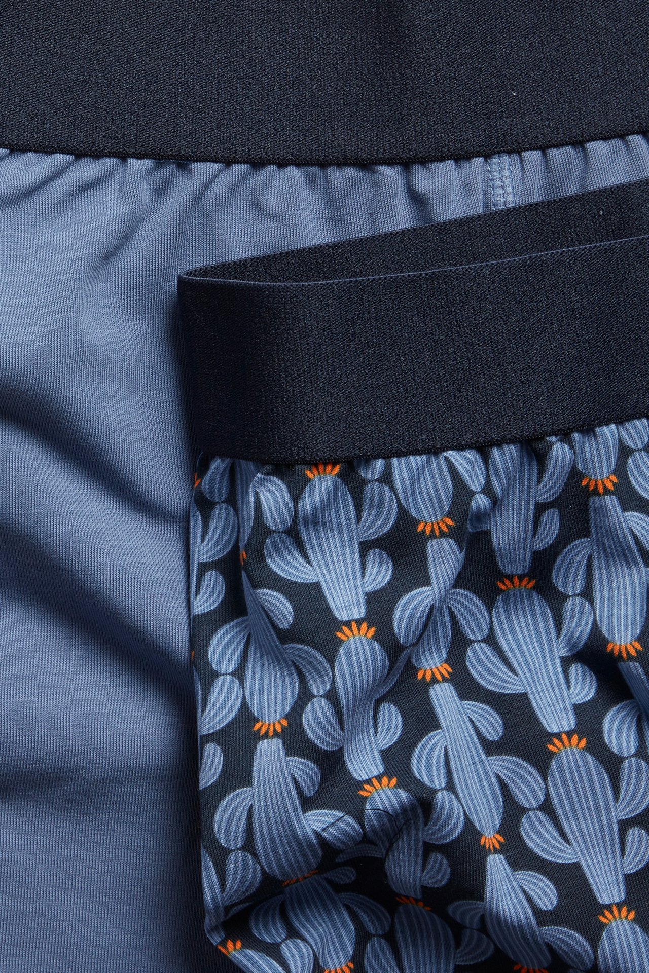 Närbild på mönstrade mörkblå boxershorts med ljusblå kaktusar, bredvid ett enfärgat ljusblått par.