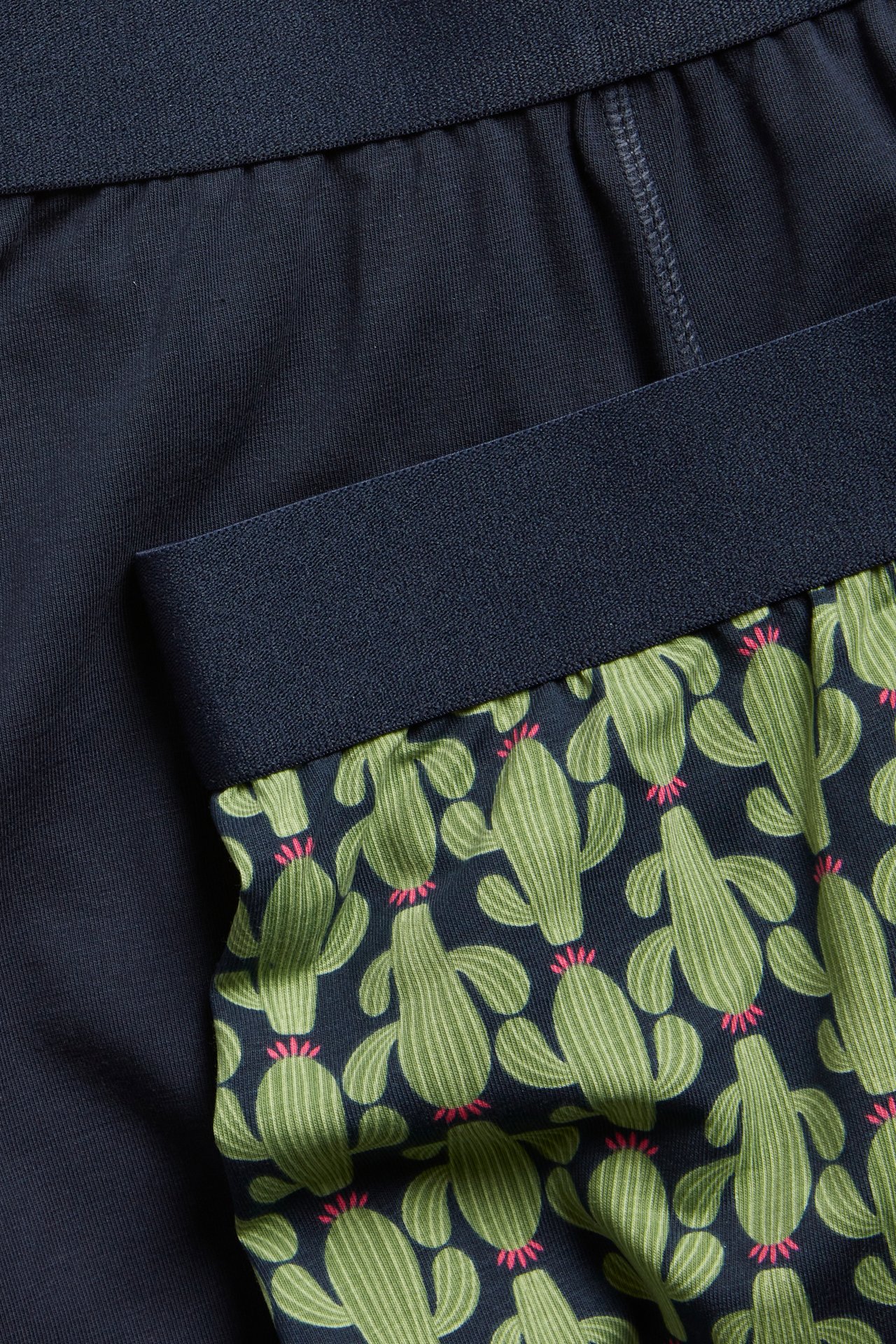 Närbild på herrboxerkalsonger i tvåpack: en enfärgad mörkblå och en mörkblå med grönt kaktusmönster.