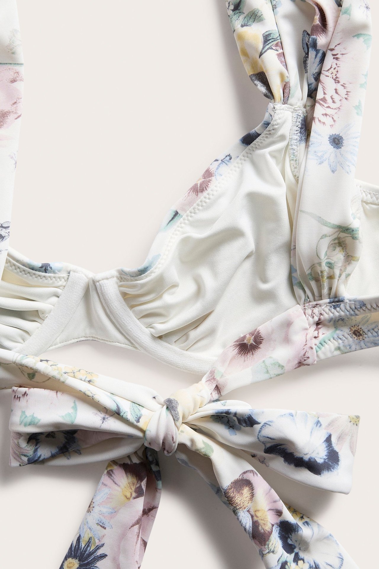 Nærbilde av en offwhite blomstret bøyle-bikinitopp med knyting i ryggen.