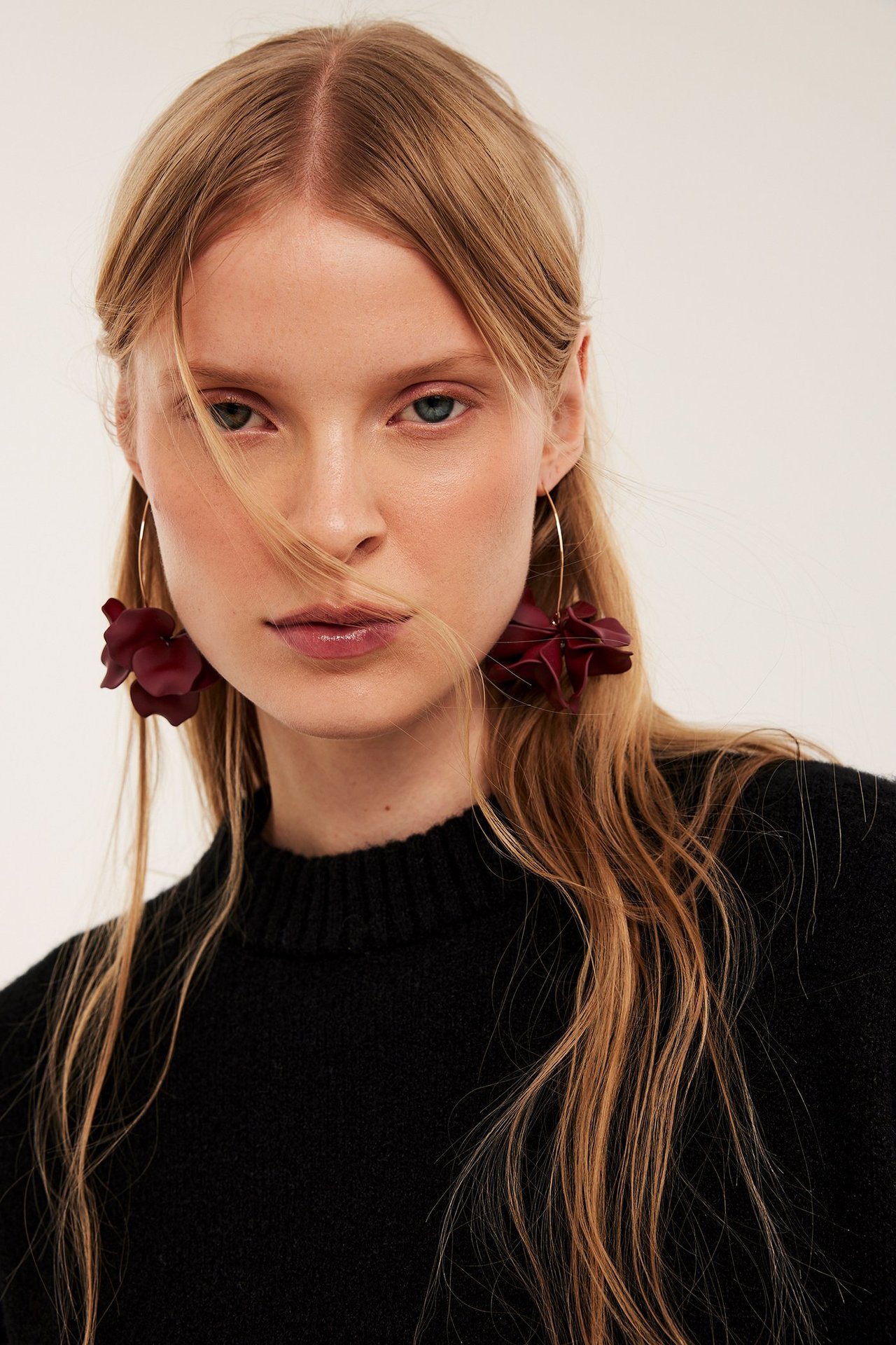 Nærbilde av en kvinne med lange røde blomsterøreringer og en svart genser.