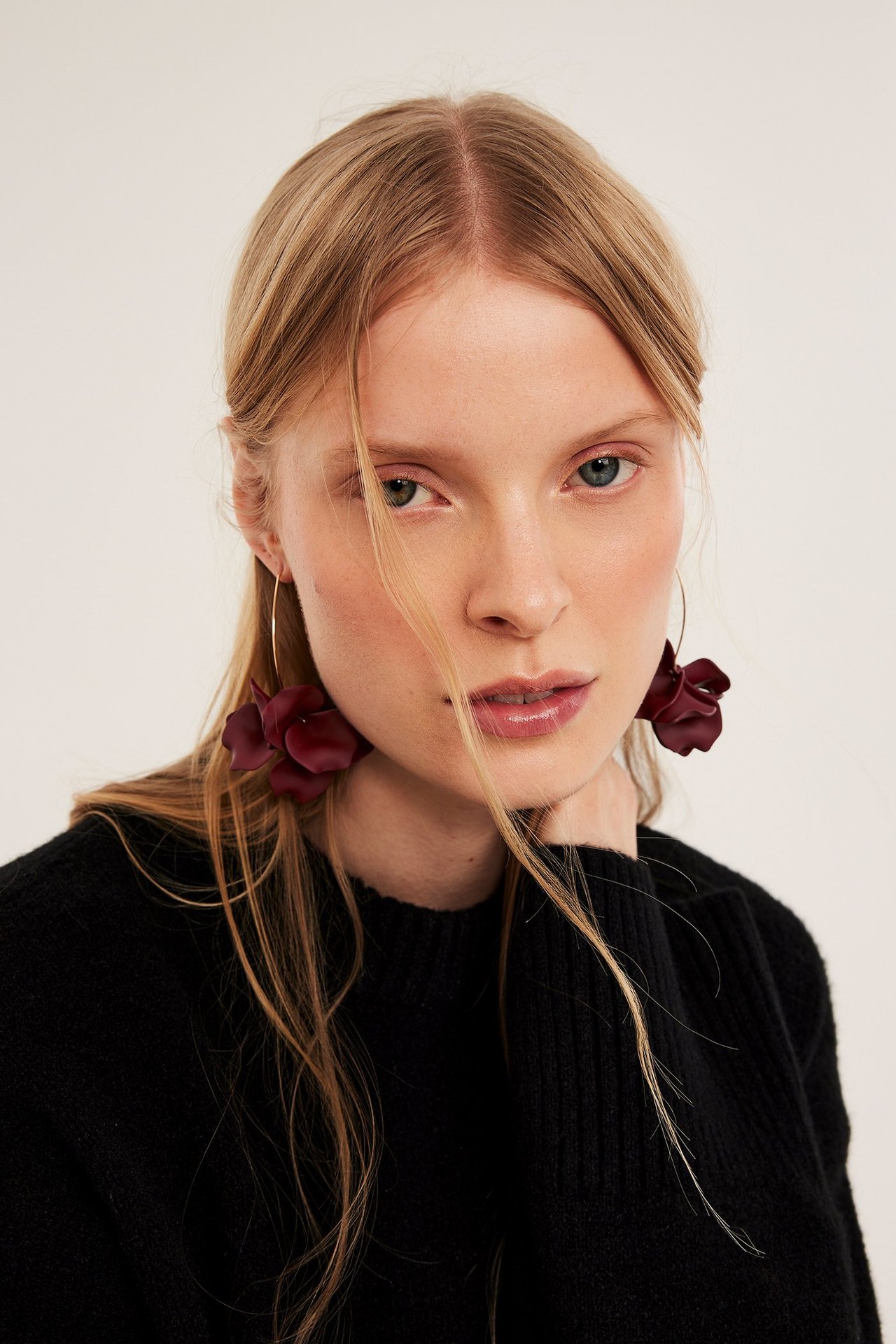 Nærbilde av kvinne med lange røde blomsterøreringer med gullringer og en svart genser.