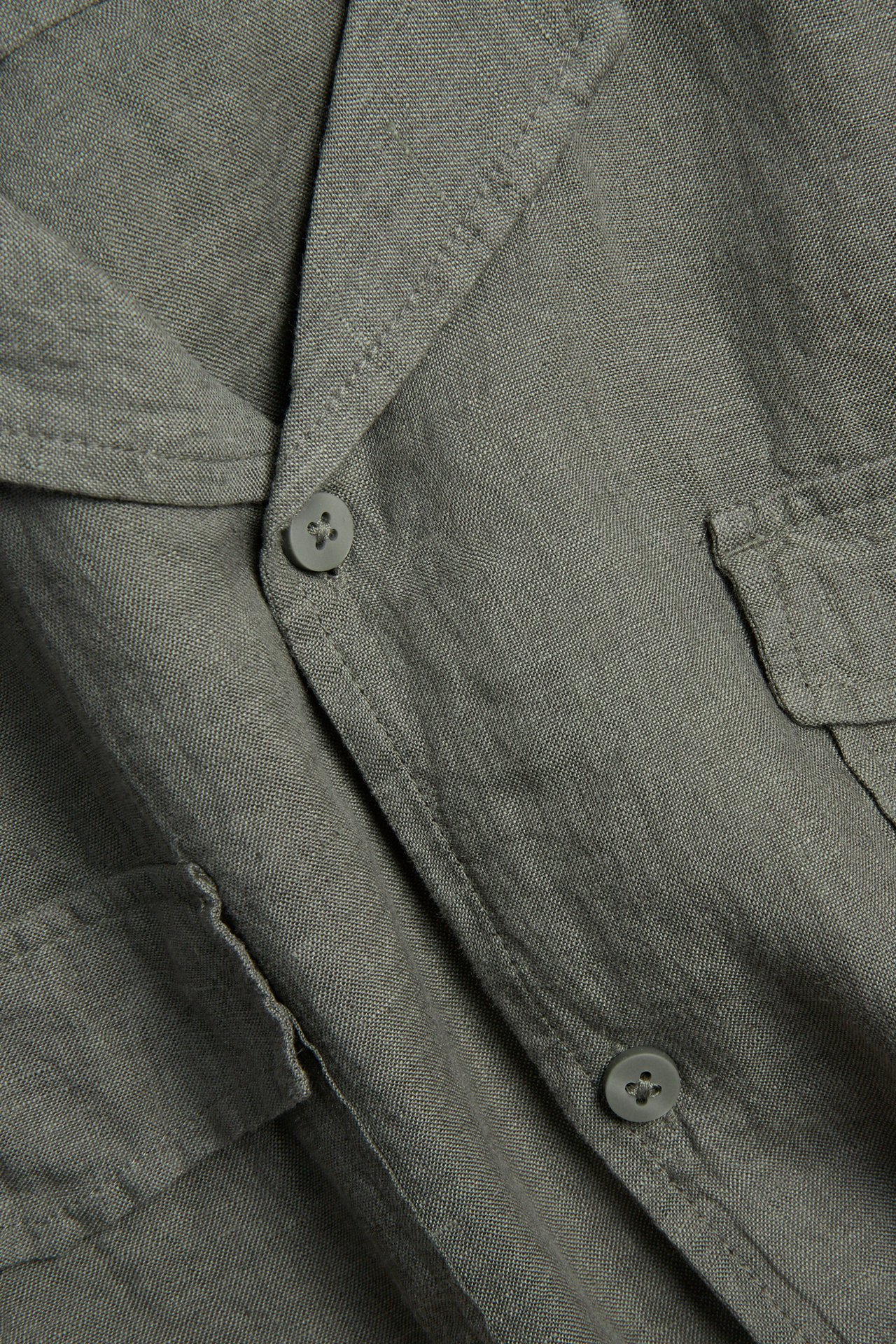 Nærbilde av en grønn melert kortermet linskjorte for menn med resortkrage, to brystlommer og knapper.