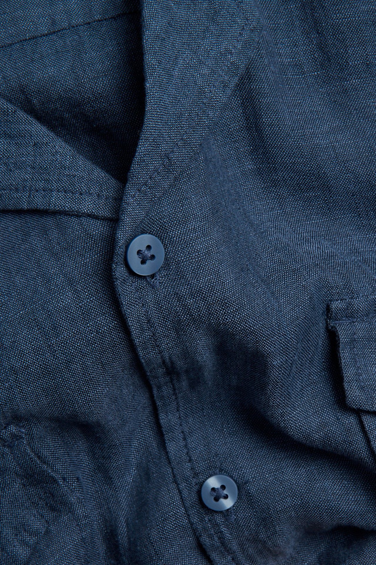 Lähikuva sinisestä kirjavasta lyhythihaisesta pellavapaidasta, jossa siniset napit ja rintatasku.