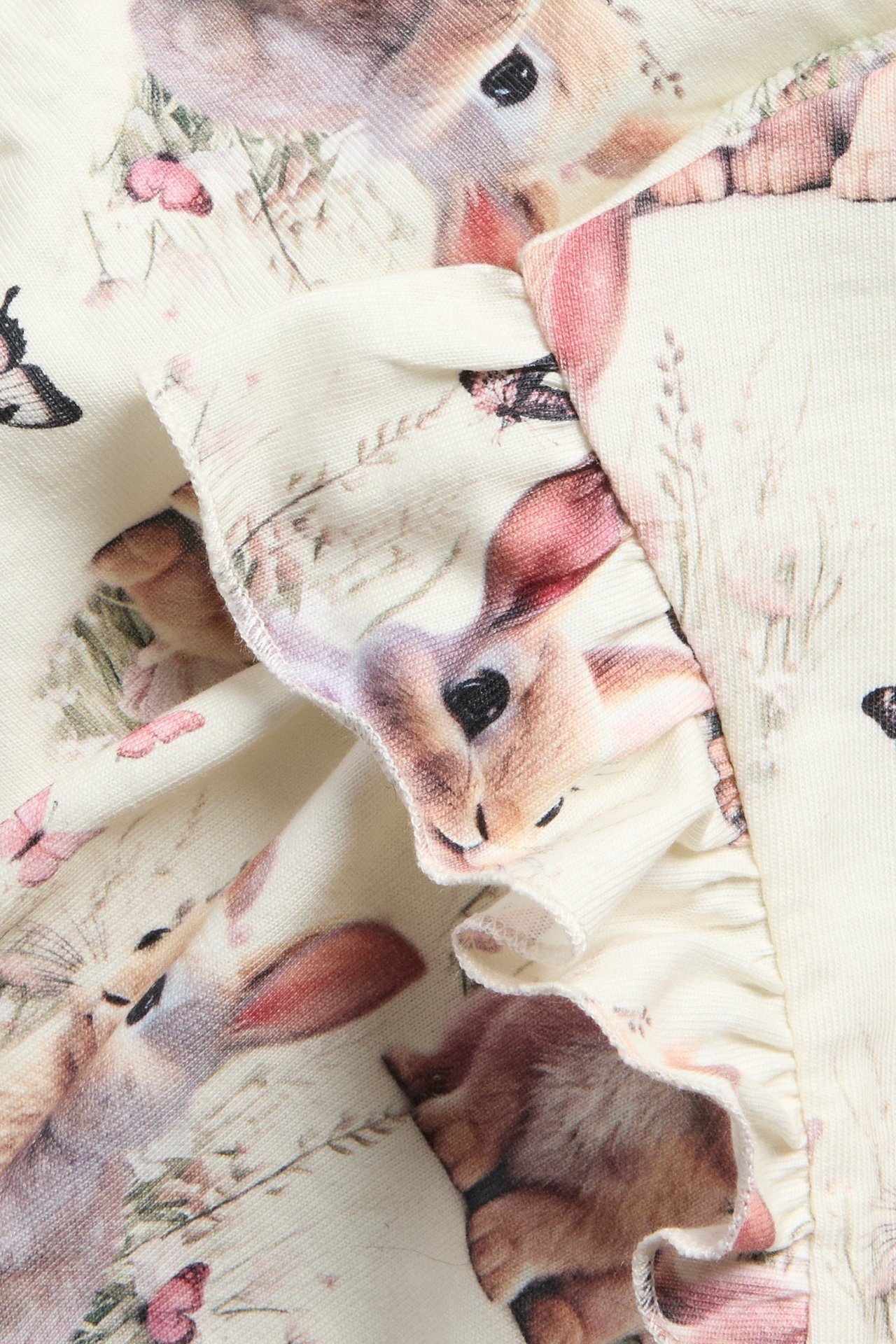 Zbliżenie na off-white bawełnianą bluzę z wzorem w króliki i kwiaty, z falbanką.