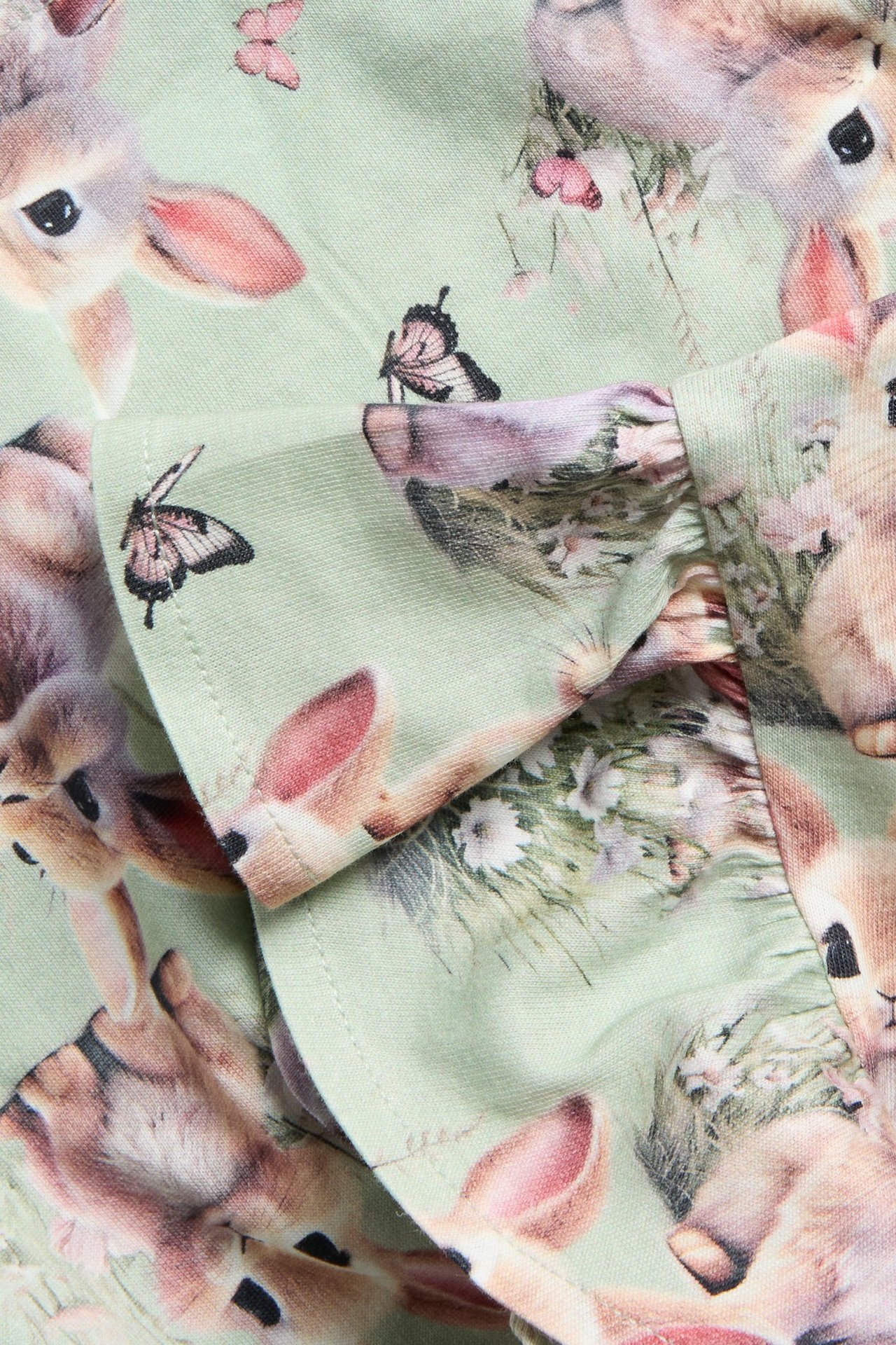 Zbliżenie zielonej bawełnianej sukienki dżersejowej z falbanami, we wzór królików i motyli.