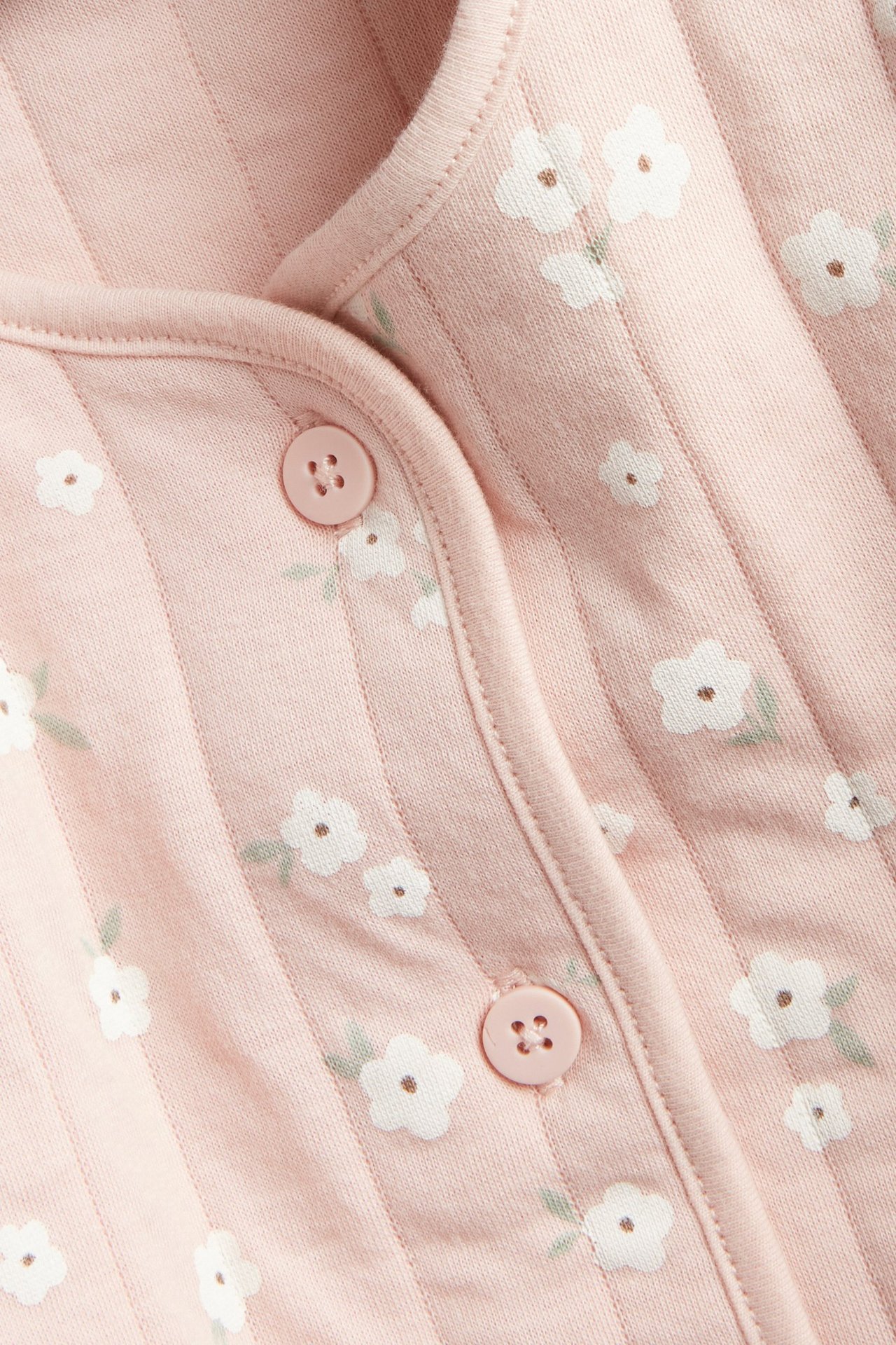 Nærbilde, forfra, av en rosa vattert babyjakke med hvitt blomstermønster og rosa knapper.