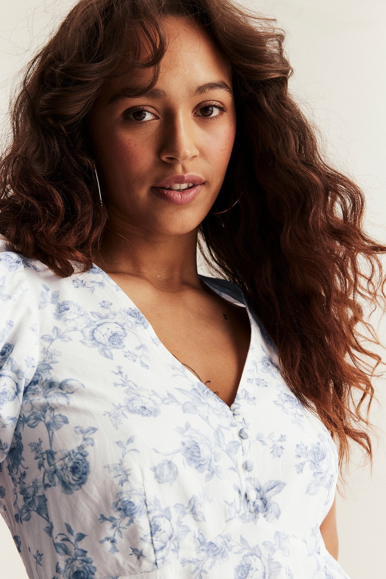 Zbliżenie od przodu na kobietę w ecru sukience w kwiaty z niebieskim wzorem, guzikami i bufiastymi rękawami.