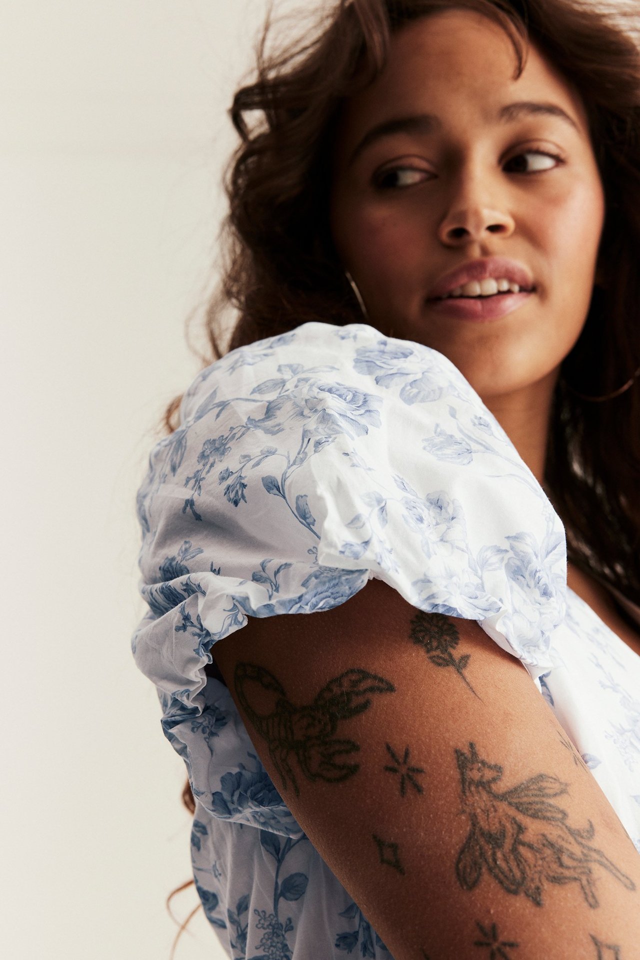 Zbliżenie kobiety w białej sukience z niebieskim wzorem kwiatowym i bufiastymi rękawami.