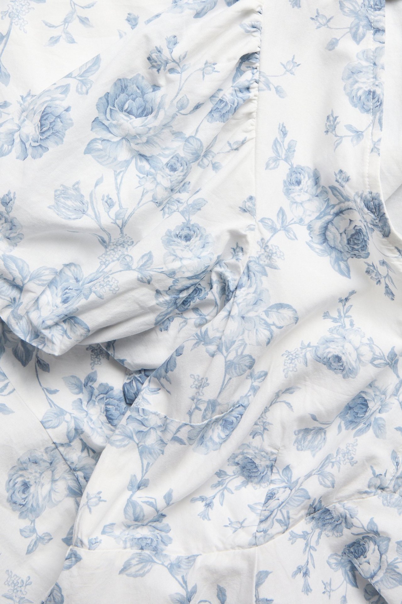 Nærbilde av en offwhite bomullskjole for dame med lyseblått blomstermønster, som viser en puffermedetalj.