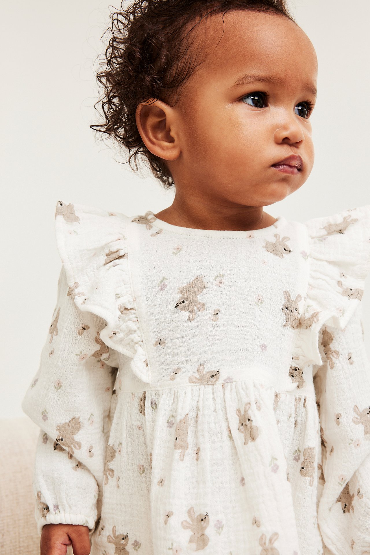 Lähikuva sivukuva vauvasta luonnonvalkoisessa harsopuserossa rypytyksillä ja ruskealla pupukuvioinnilla.