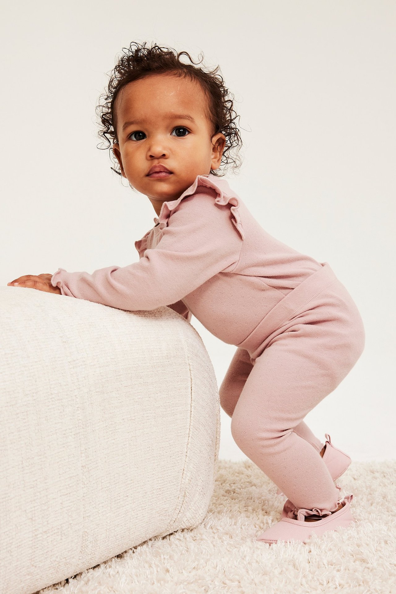 Sivukuva vauvasta yllään vaaleanpunainen pointelle-body röyhelöillä, yhteensopivat leggingsit ja kengät.