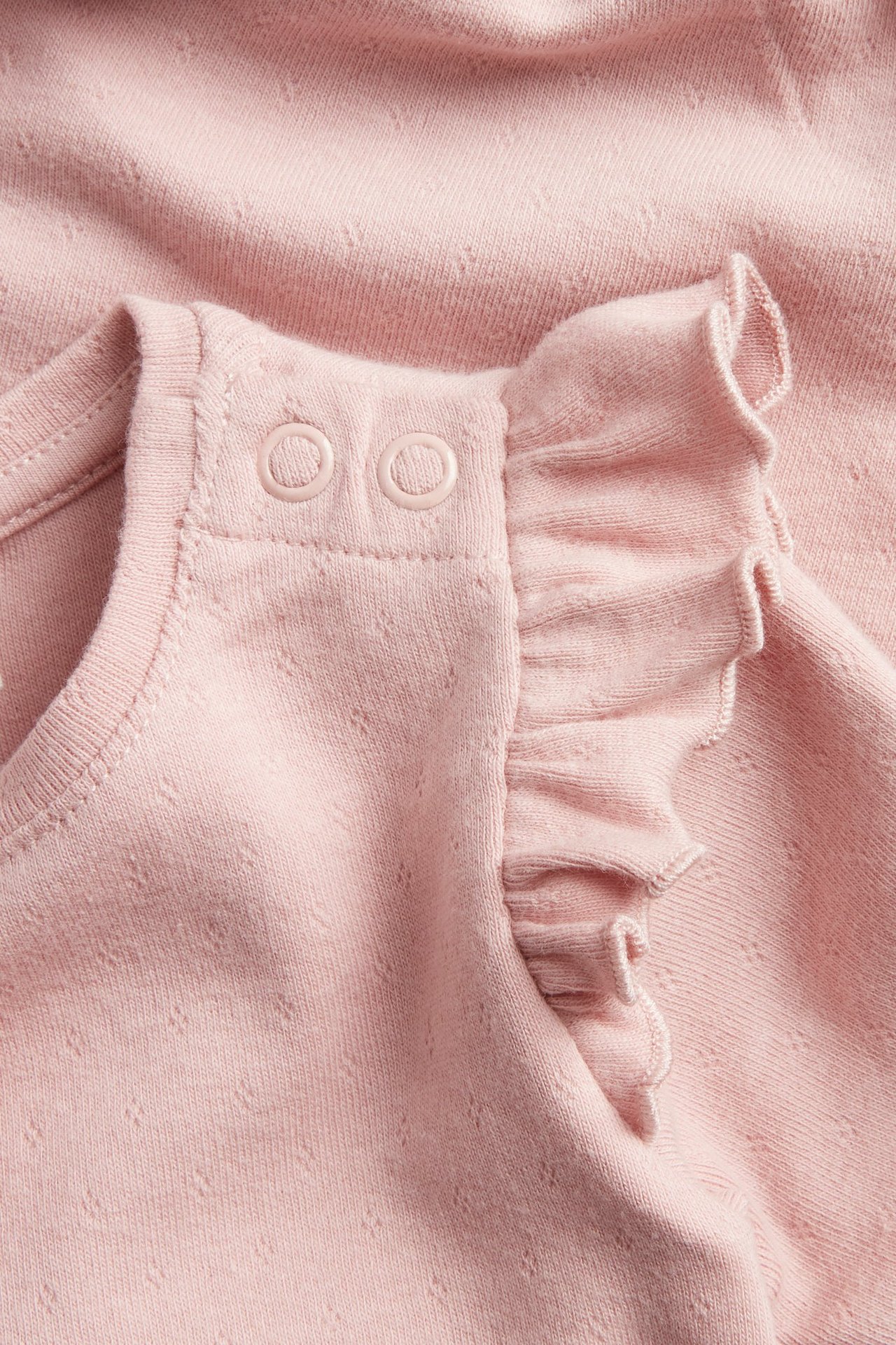 Zbliżenie różowego body niemowlęcego pointelle z napami na ramieniu i falbankami na rękawach.