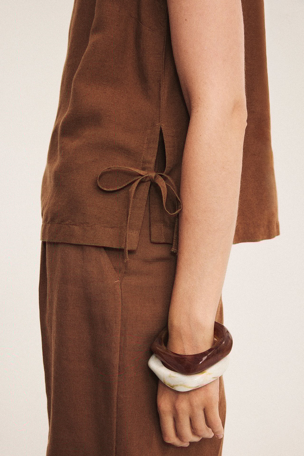 Zbliżenie kobiety noszącej dwie marmurkowe plastikowe bransoletki: beżową, ciemnobrązową, z brązowym topem i spodniami.