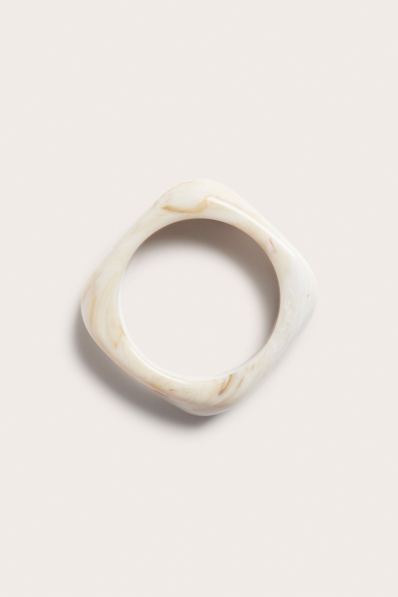 Toppvy av ett ljusbeige plastarmband med melerat marmorutseende och rundad-fyrkantig form.