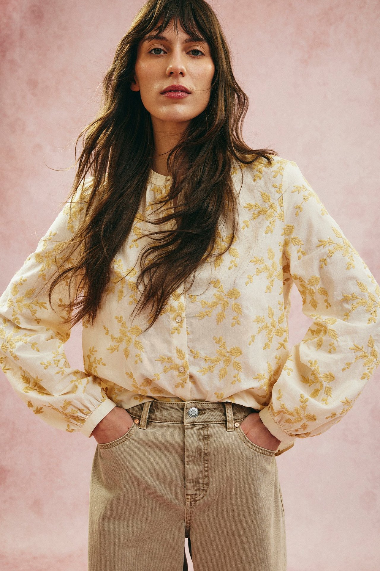 Forfra: kvinne i lys gul bluse med broderi, knapper og beige vide jeans.