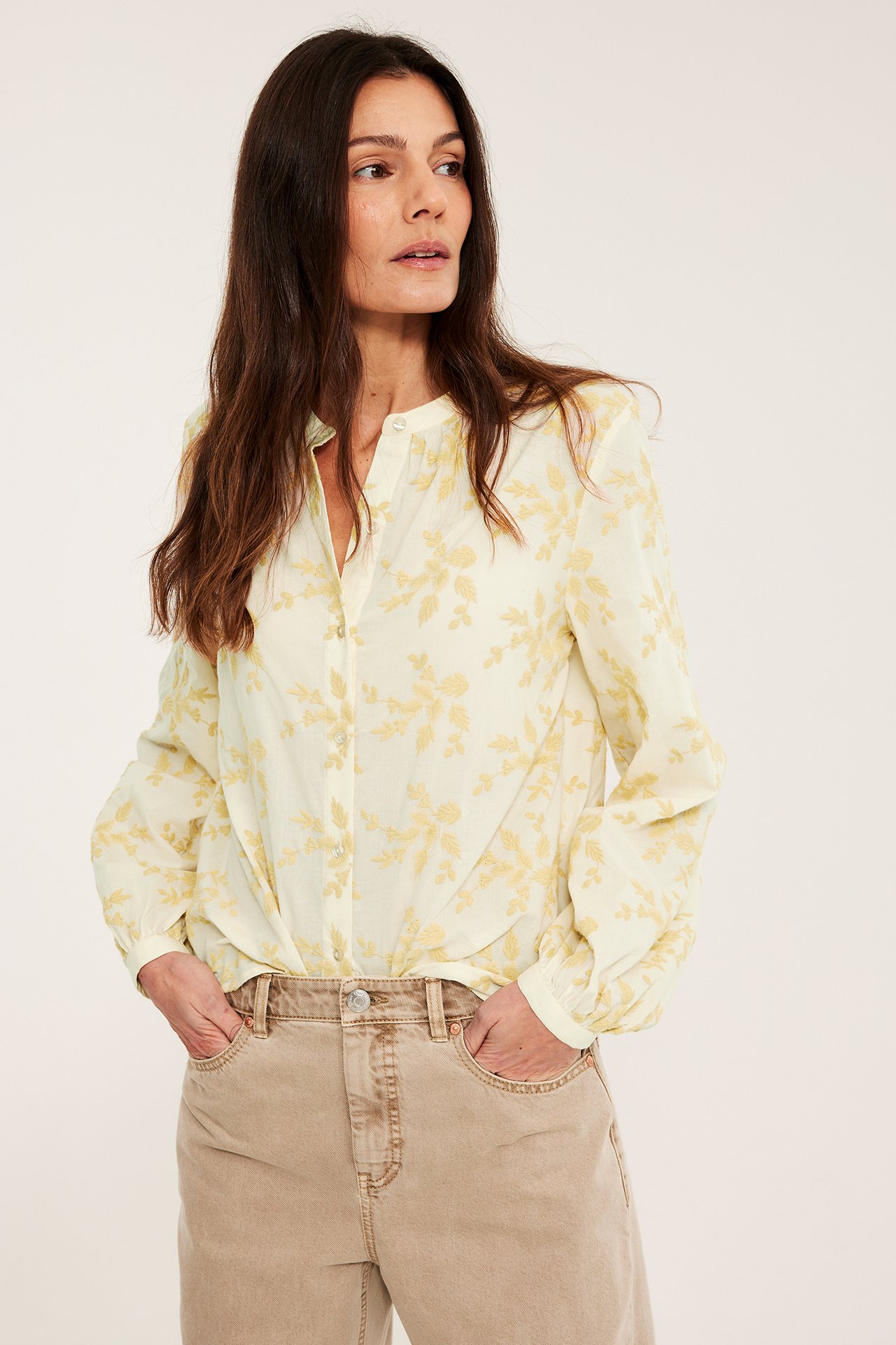 Frontbilde av kvinne i lys gul bomullsbluse med blomsterbroderi og beige bukser.