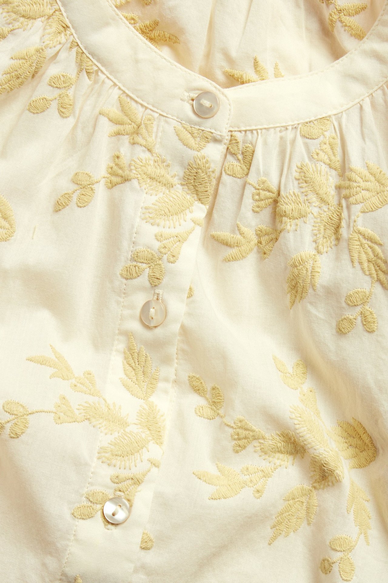 Zbliżenie na jasnożółtą bawełnianą bluzkę z jasnożółtym kwiatowym haftem i białymi guzikami.