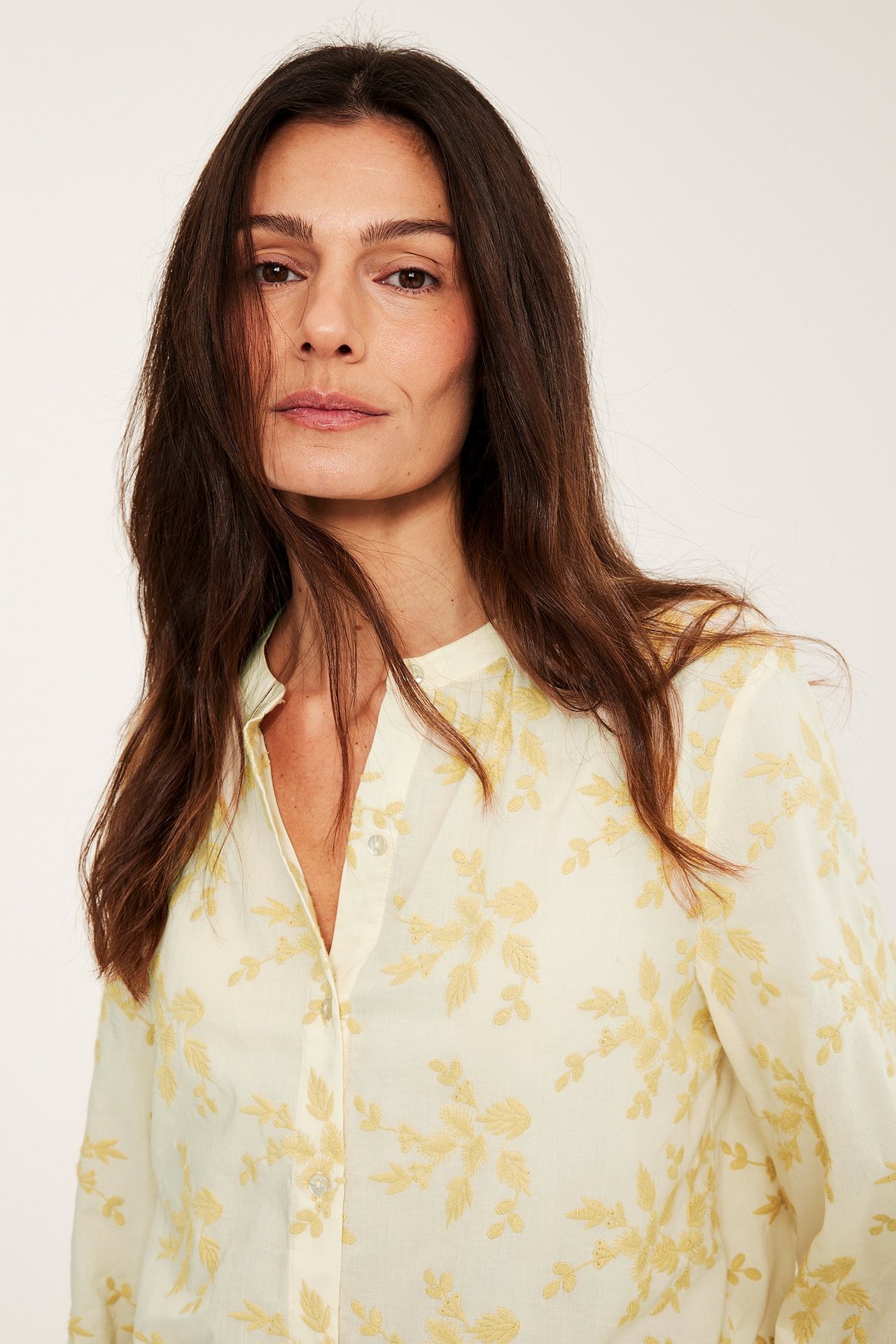 Nærbilde av kvinne i lys gul bomullsbluse med broderte blomstermønstre og knapper.