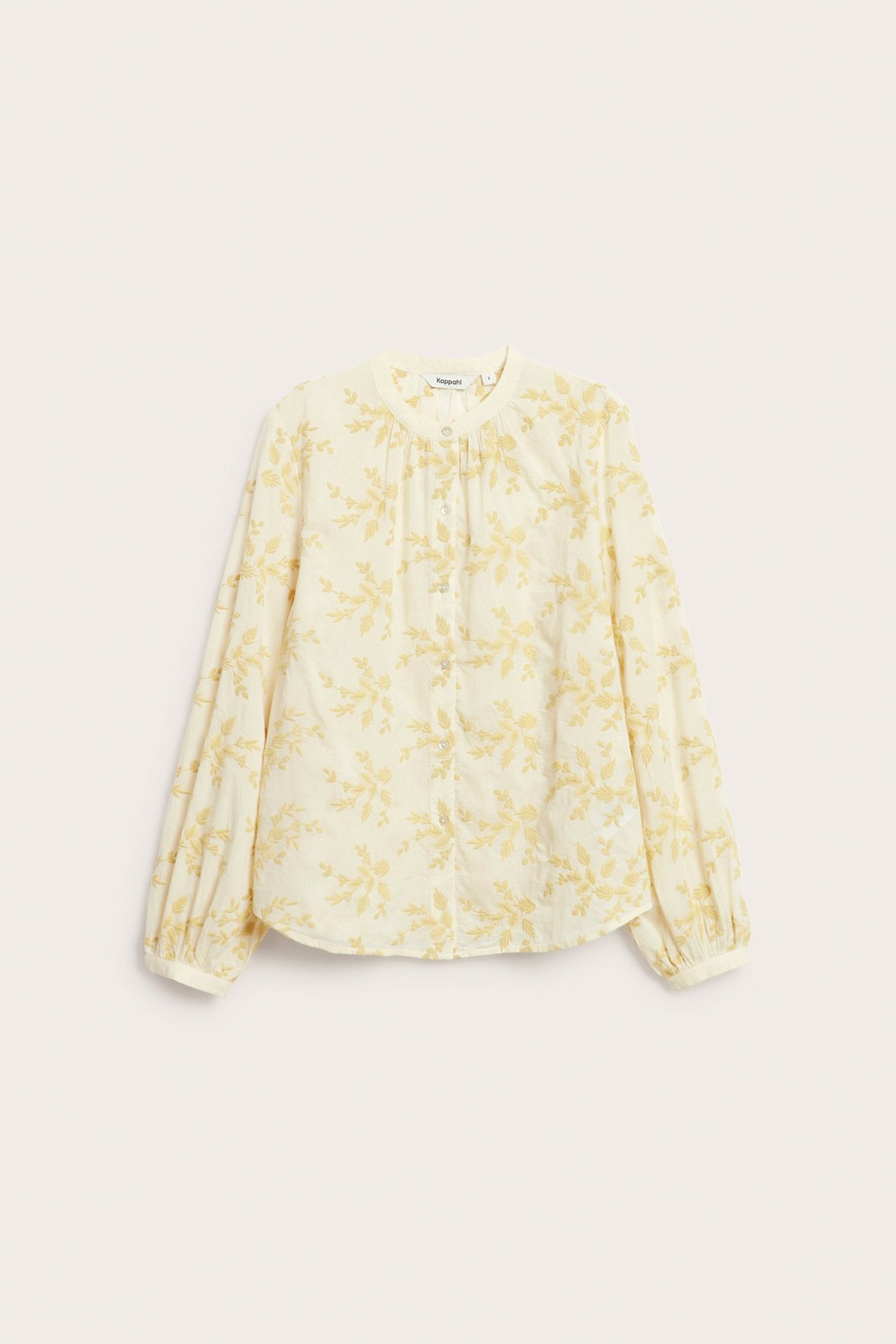 Edestä: naisen kermanvärinen puuvillapusero, keltainen kukkakirjonta, pyöreä pääntie, nappikiinnitys.