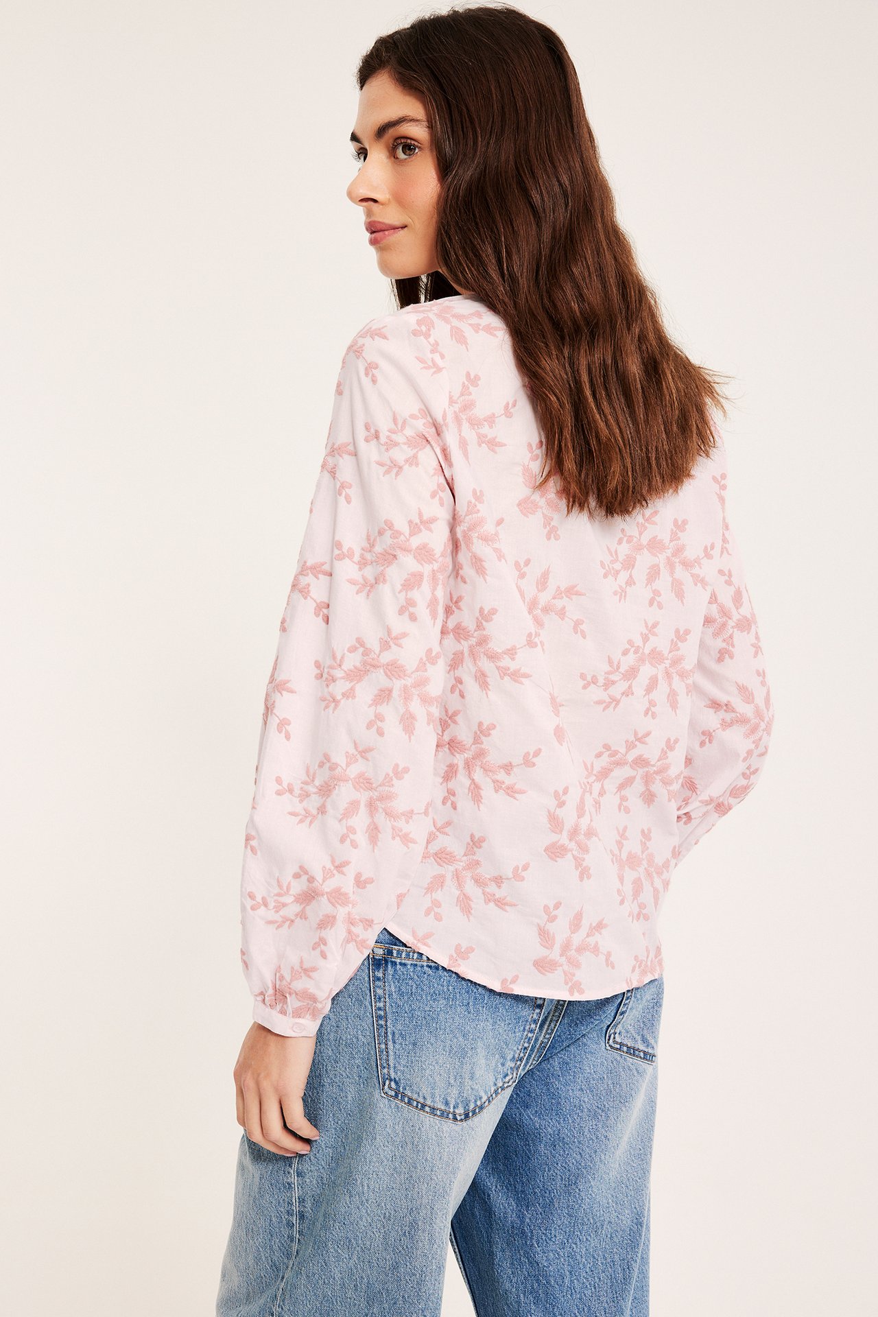 Sidovy av kvinna i en ljusrosa bomullsblus med broderade blommor och blå jeans.