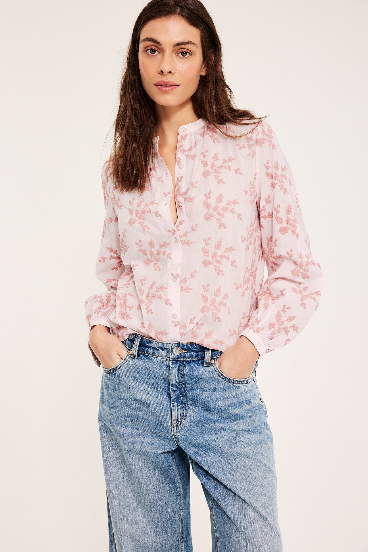 Framifrån, kvinna i ljusrosa broderad bomullsblus och ljusblå löst sittande jeans.
