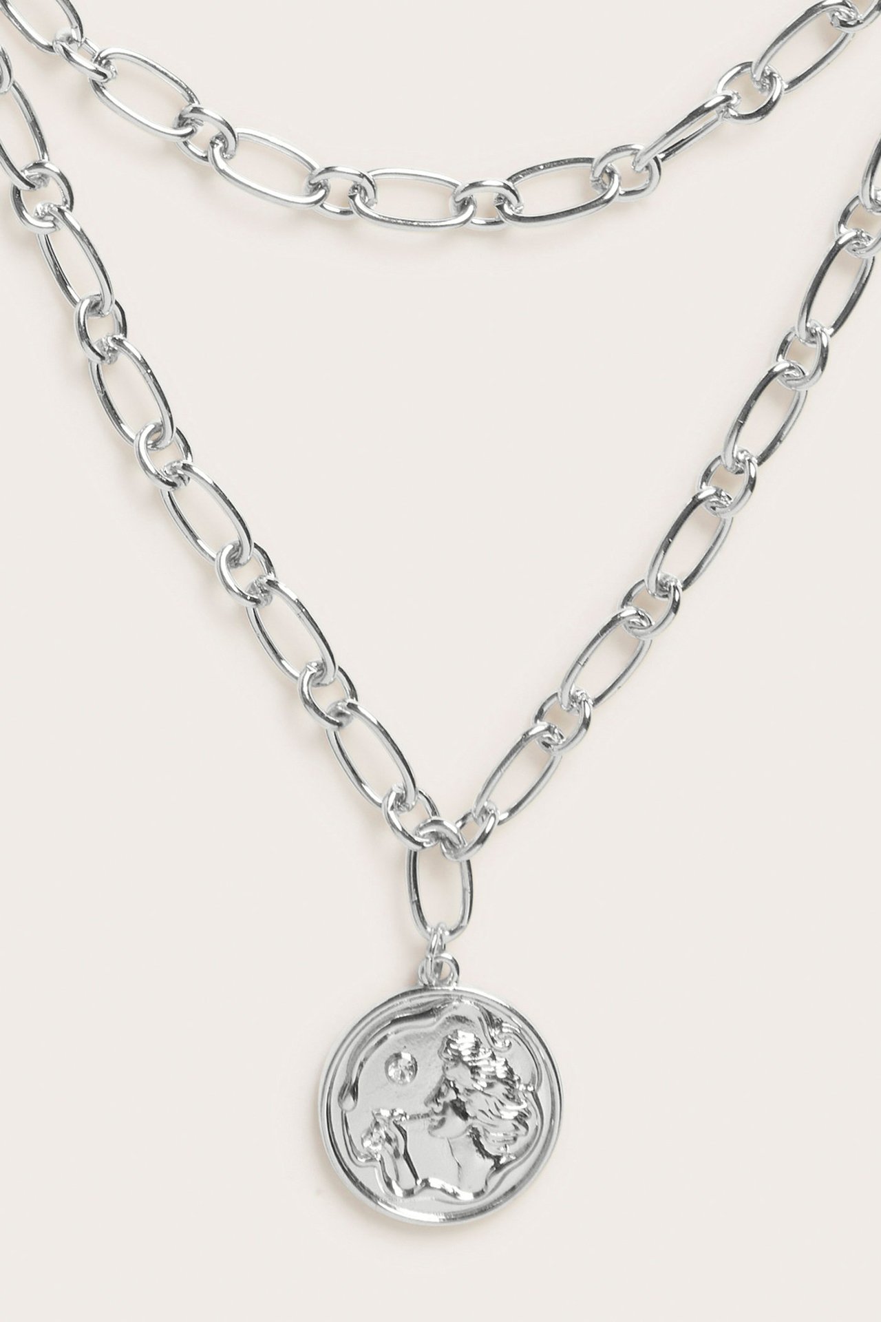 Närbild framifrån av silverfärgat metallhalsband med två kedjor och runt medaljonghänge.