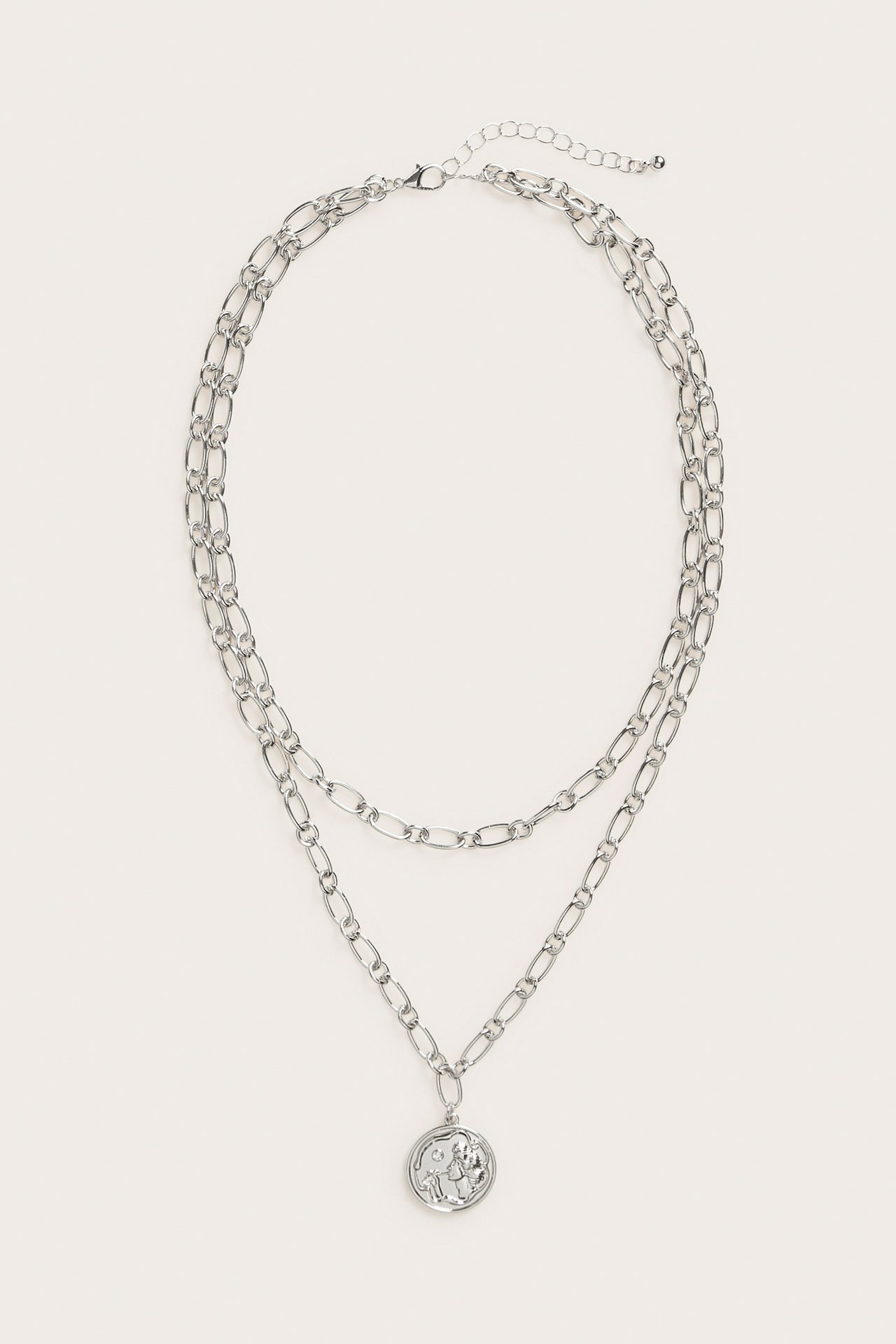 Framifrån, silverfärgat dubbelkedjehalsband med runt dekorativt hänge och justerbart lås.