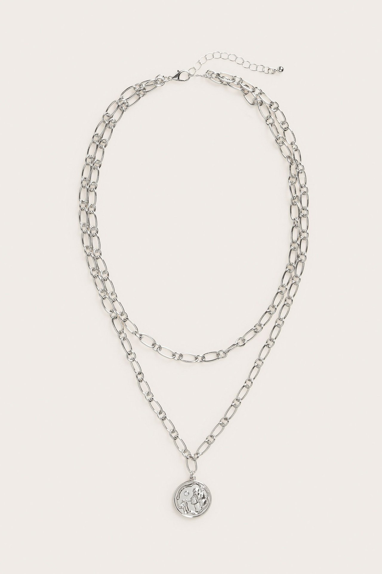 Framifrån, silverfärgat dubbelkedjehalsband med runt dekorativt hänge och justerbart lås.