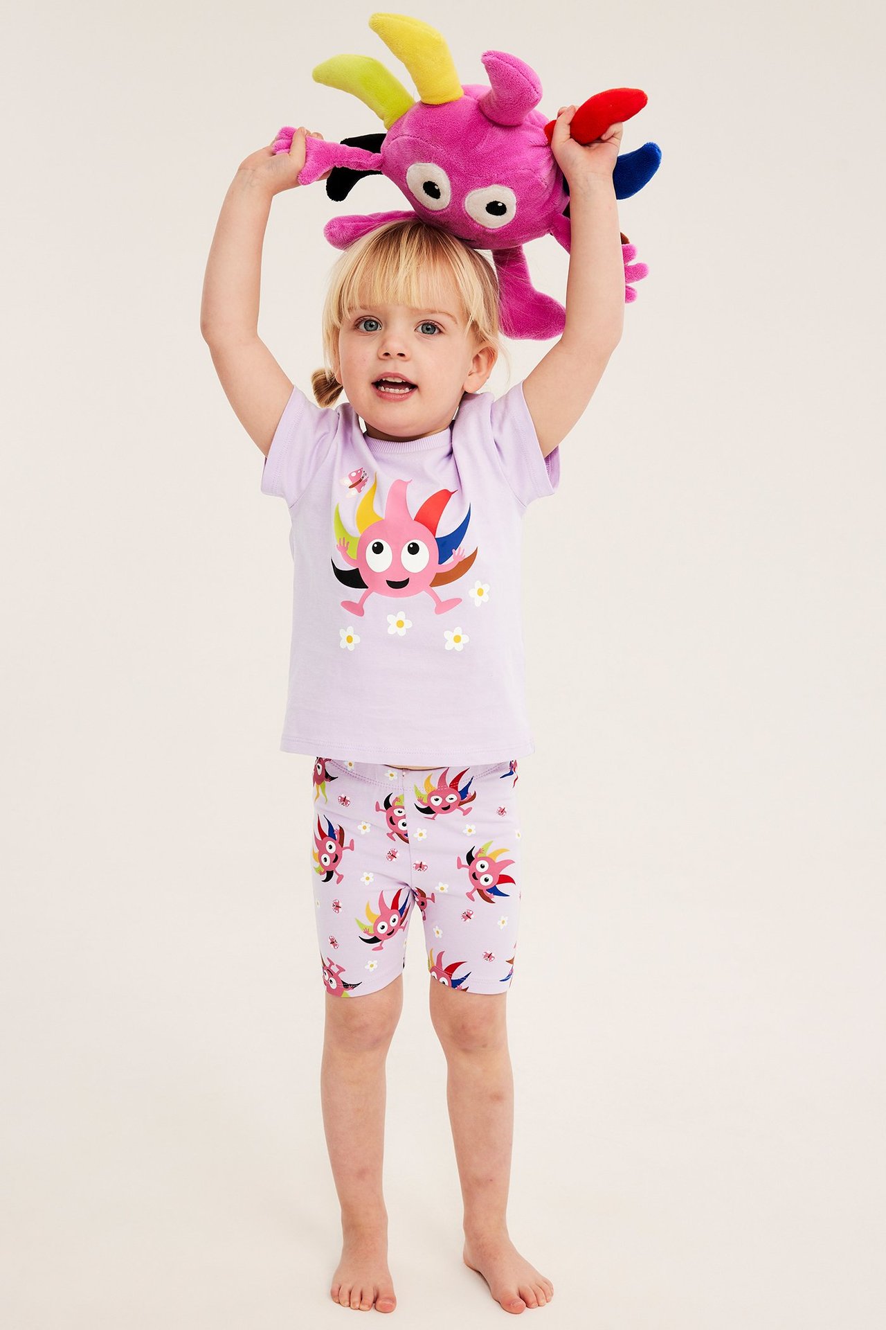 Widok z przodu: dziecko w liliowych szortach Babblarna i pasującej koszulce, trzyma różową pluszową zabawkę.
