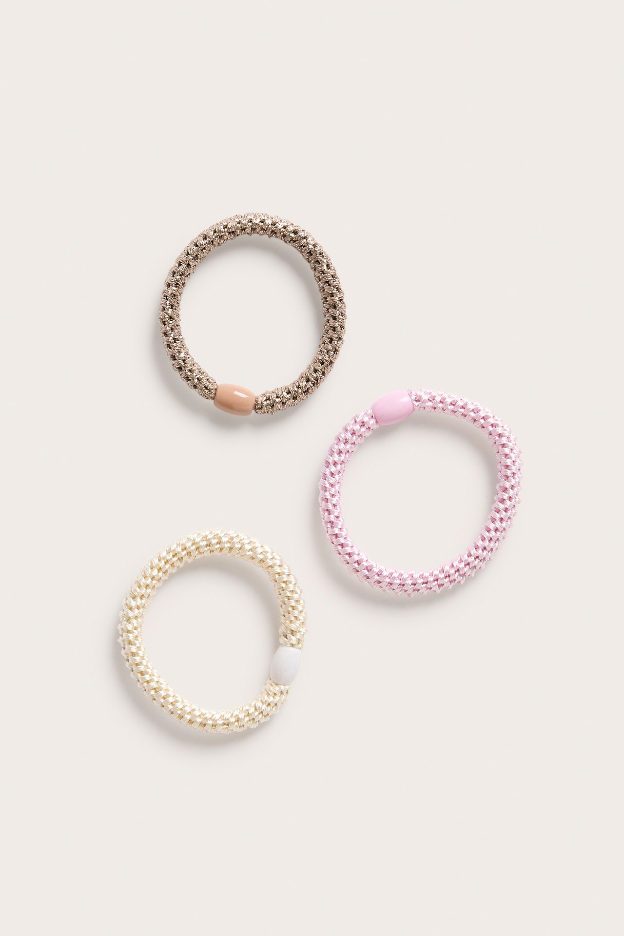 Överblick av tre tjocka, elastiska hårsnoddar: rosa, ljusbeige och krämfärgad, med matchande plastpärlor.