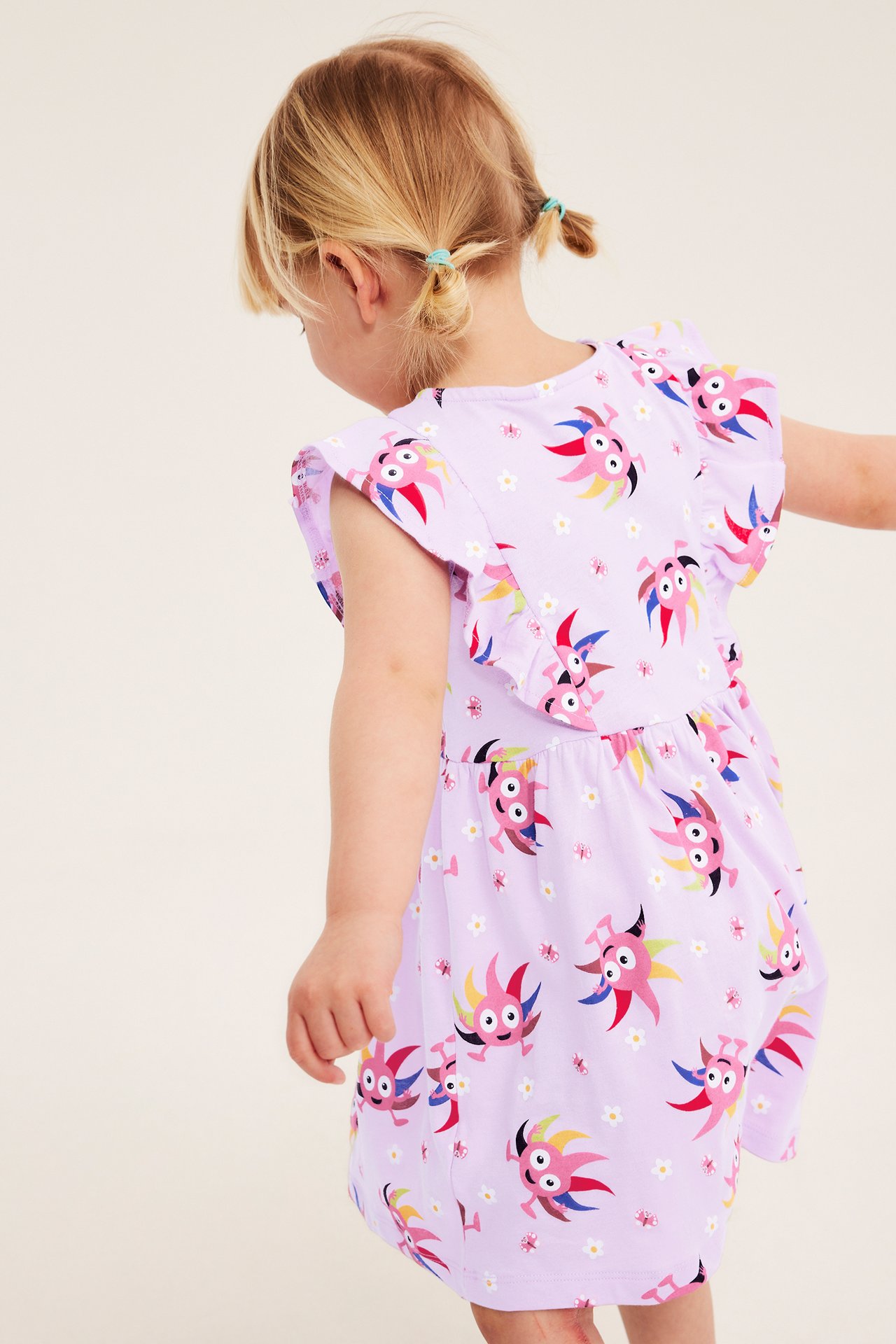Bakifrån på ett barn i lila bomullsklänning med Diddi-tryck och volangärmar.