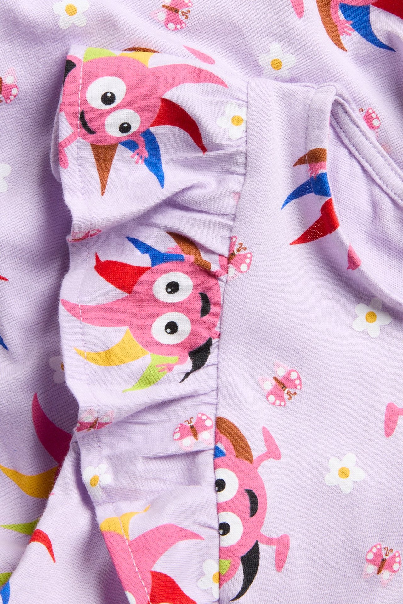 Lähikuva lasten lila puuvillamekosta, jossa värikäs Diddi- ja kukkakuvio sekä röyhelö.