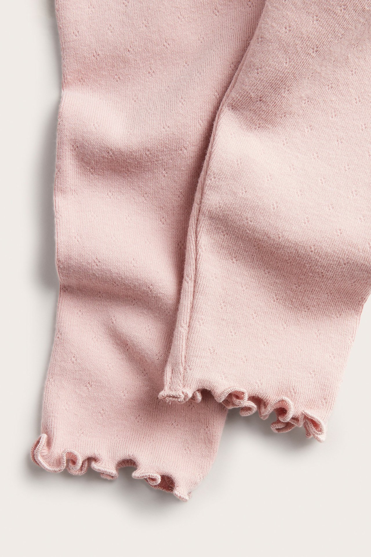 Zbliżenie na różowe, pointelle dzianinowe legginsy niemowlęce z falbankowymi obszyciami.