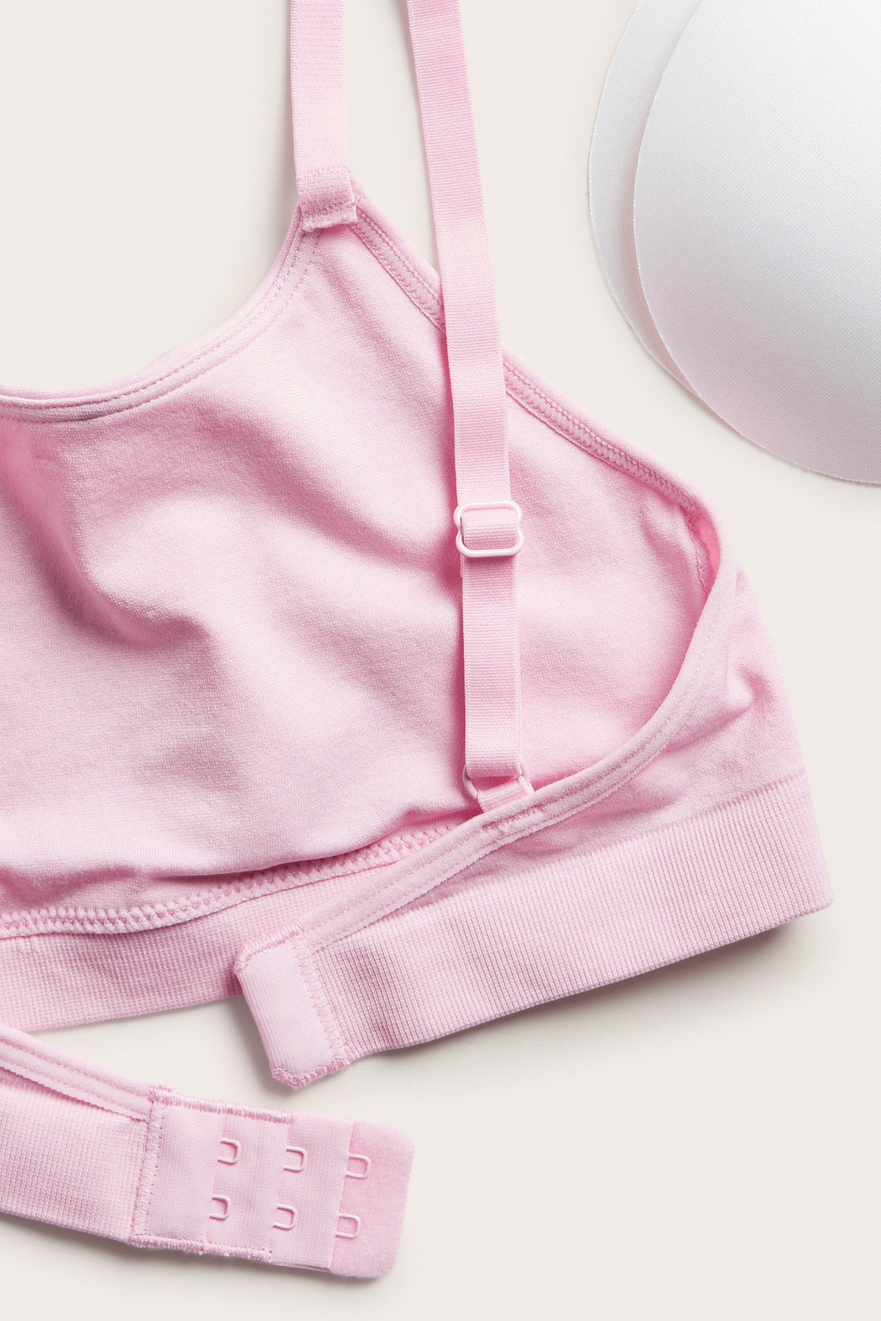Närbild av rosa sömlös behå med justerbara axelband, hyskknäppning och två vita inlägg.