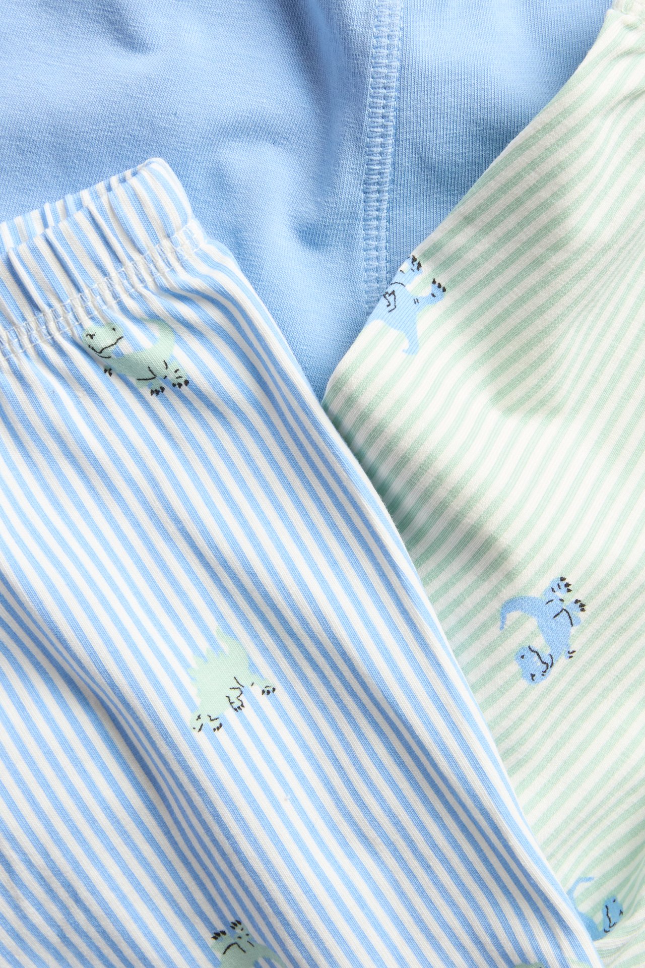 Zbliżenie na 3-pak bokserek dziecięcych: jedne jasnoniebieskie, dwa w kolorze złamanej bieli w paski i dinozaury.