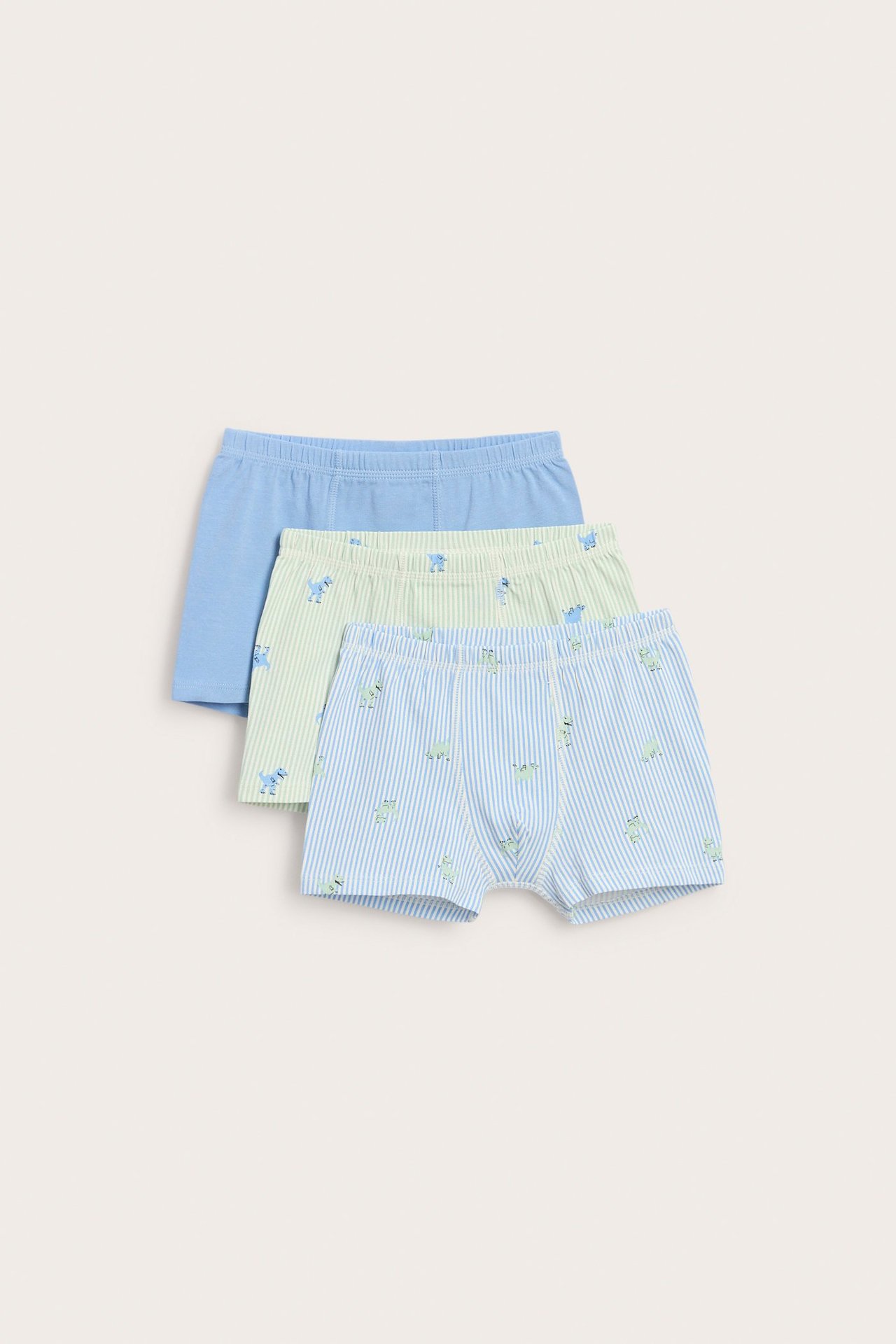 Trzy bokserki dziecięce z dinozaurami: niebiesko-białe w paski, zielono-białe w paski i jednolicie jasnoniebieskie.
