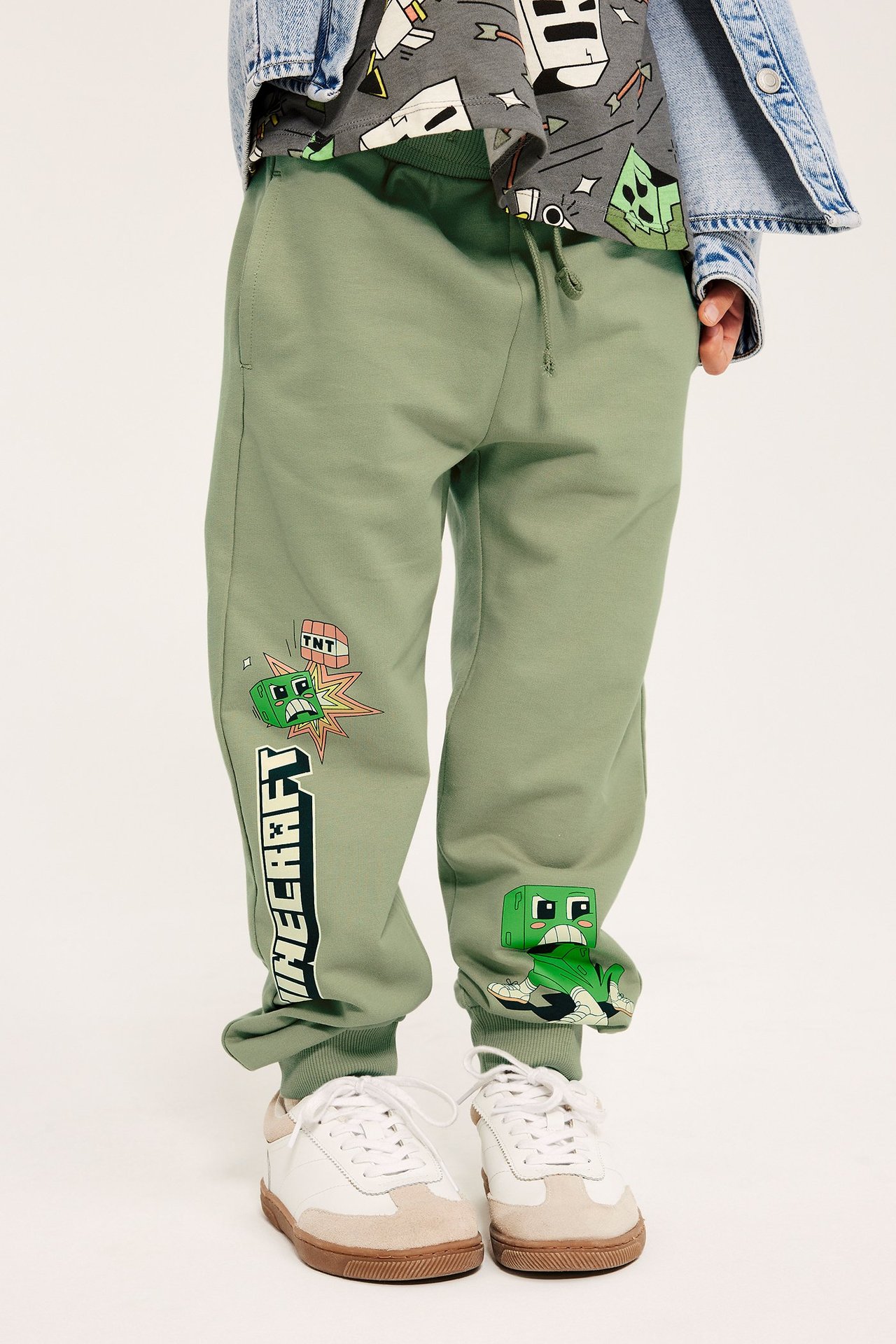 Edestä: Lapsi tummanvihreissä Minecraft-puuvillahousuissa, harmaassa t-paidassa ja farkkutakissa.