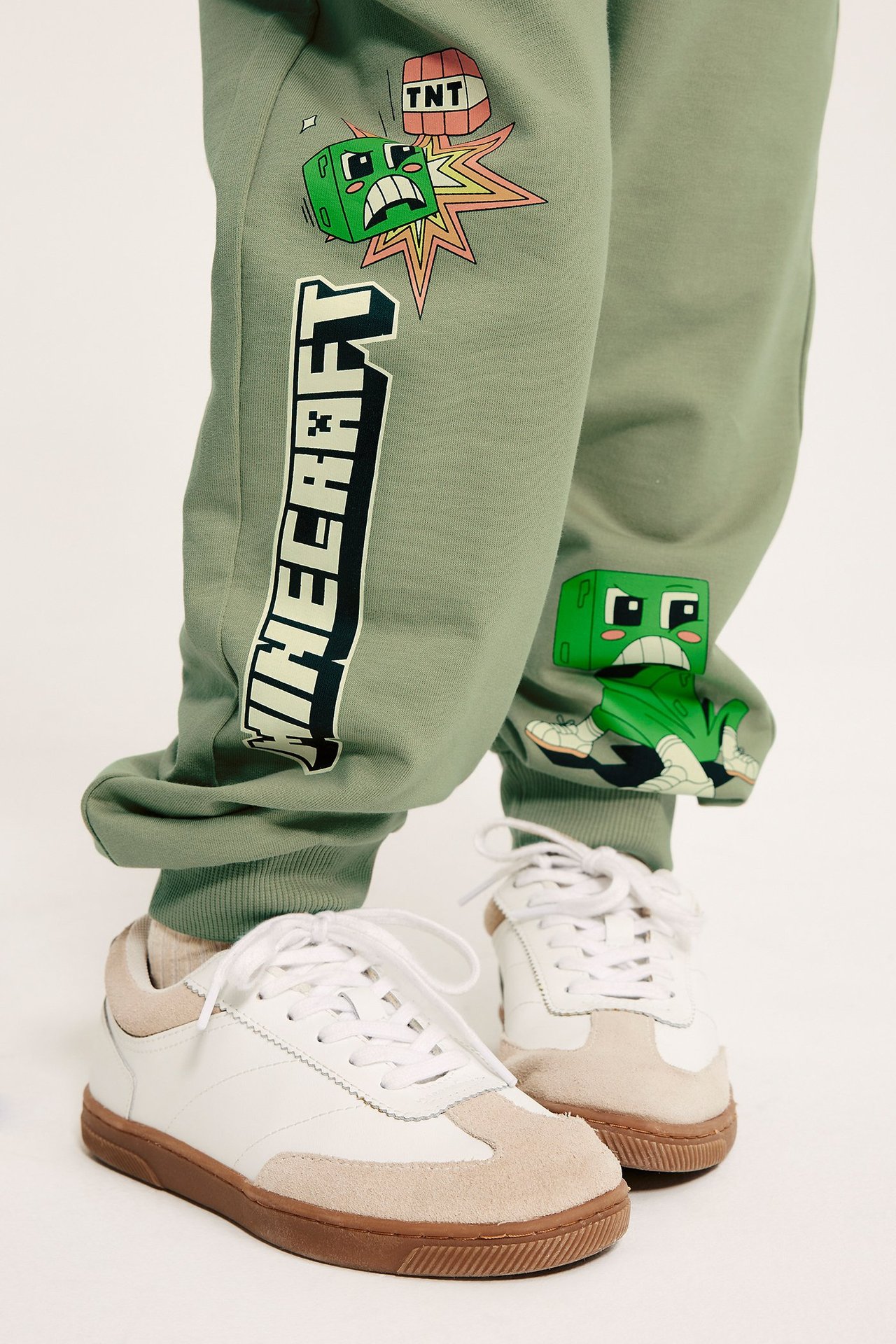 Lähikuva edestä lapsesta yllään tummanvihreät Minecraft-kuvioiset puuvillajoggerit ja valkobeiget tennarit.