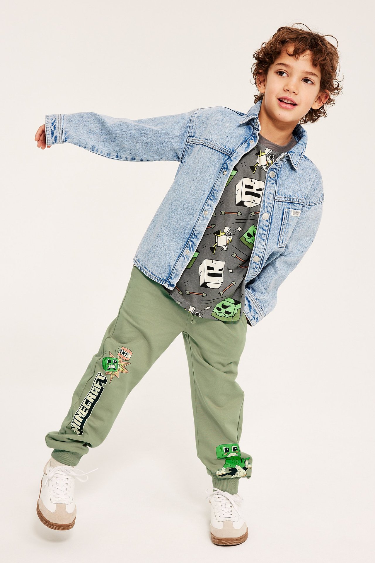 Edestäpäin kuvattu lapsi yllään tummanvihreät Minecraft collegehousut, harmaa Minecraft t-paita ja vaaleansininen farkkutakki.