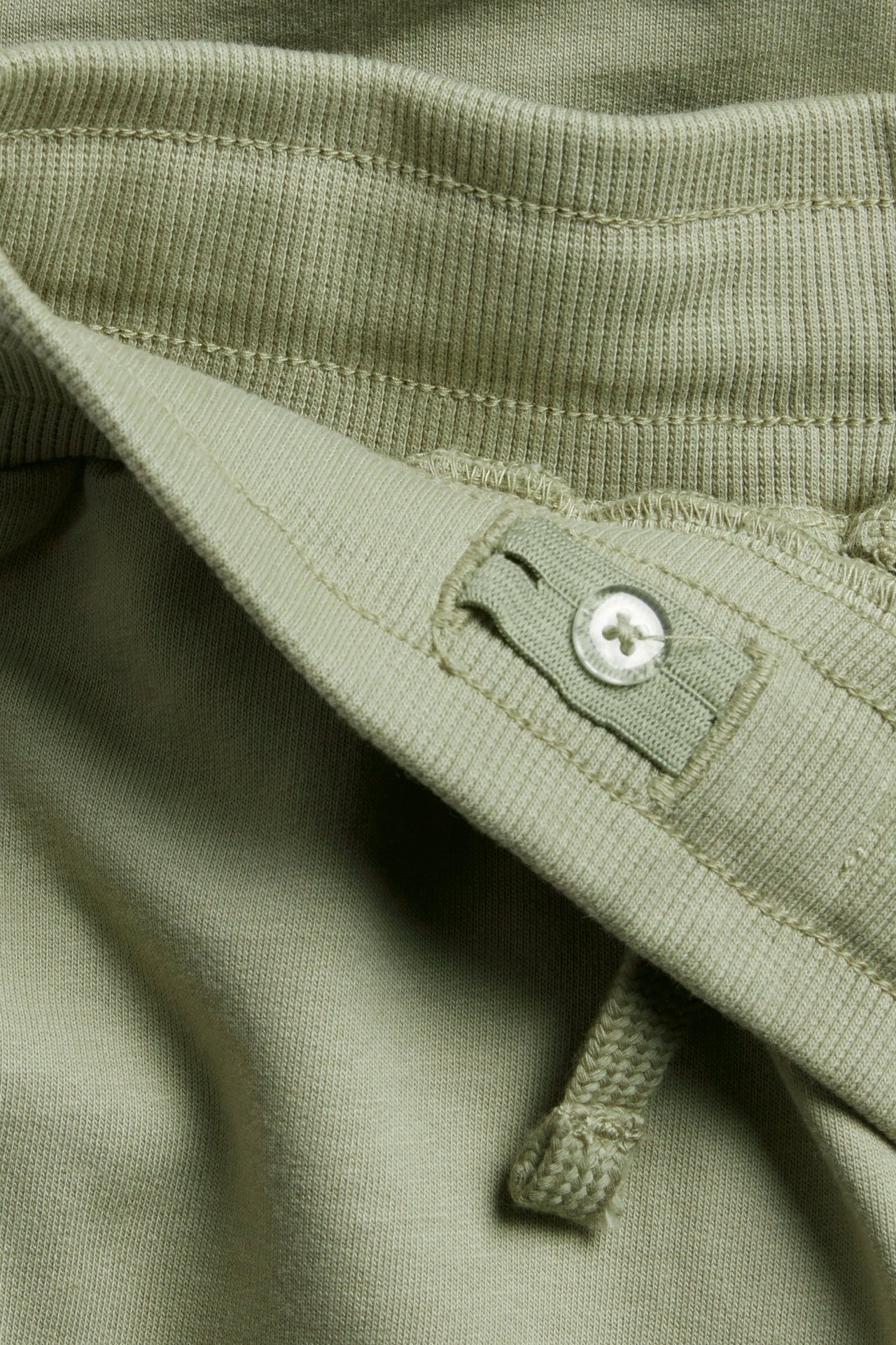 Zbliżenie na pas ciemnozielonych bawełnianych spodni dresowych ze sznurkiem i regulacją na guzik.