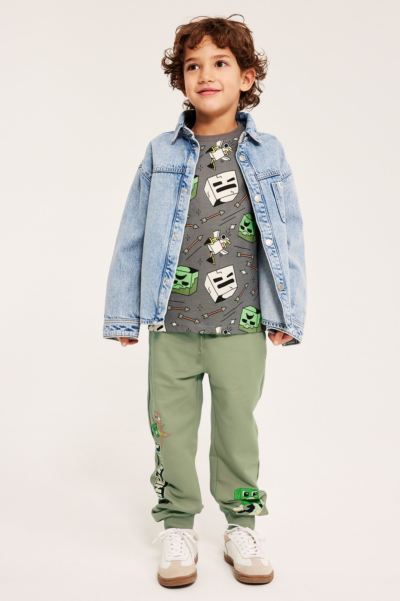 Edestä: Lapsi yllään tummanvihreät Minecraft-kuvioidut collegehousut, harmaa t-paita, vaaleansininen farkkutakki ja lenkkarit.