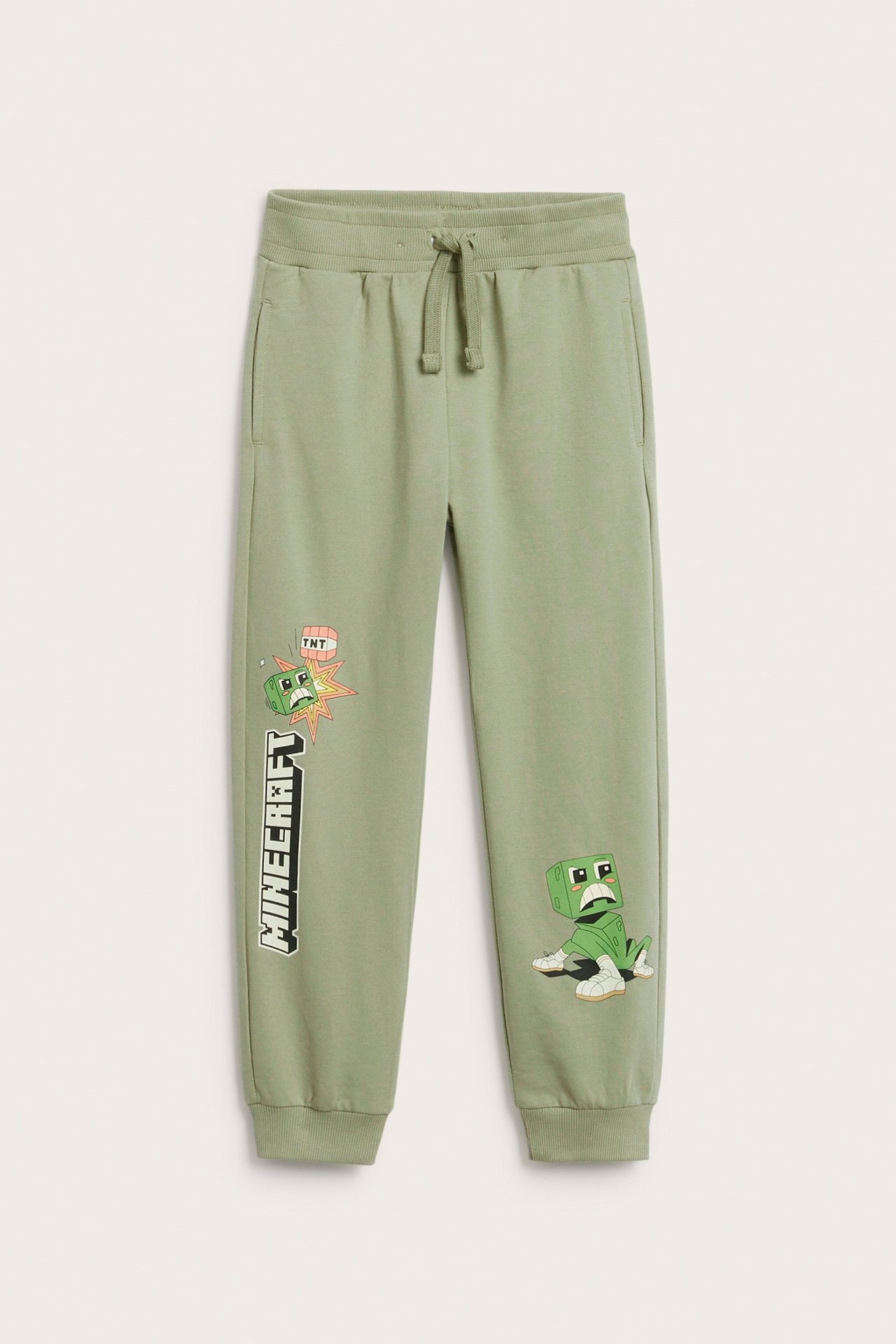 Edestä kuvatut lasten tummanvihreät Minecraft-kuvioiset puuvillajoggerit kiristysnyörillä vyötäröllä.