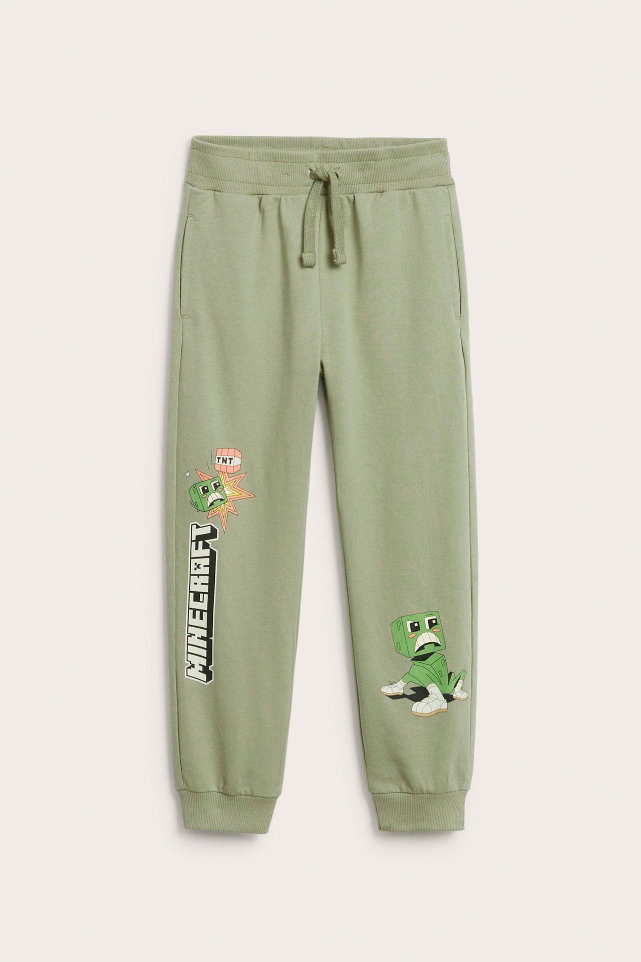 Edestä kuvatut lasten tummanvihreät Minecraft-kuvioiset puuvillajoggerit kiristysnyörillä vyötäröllä.